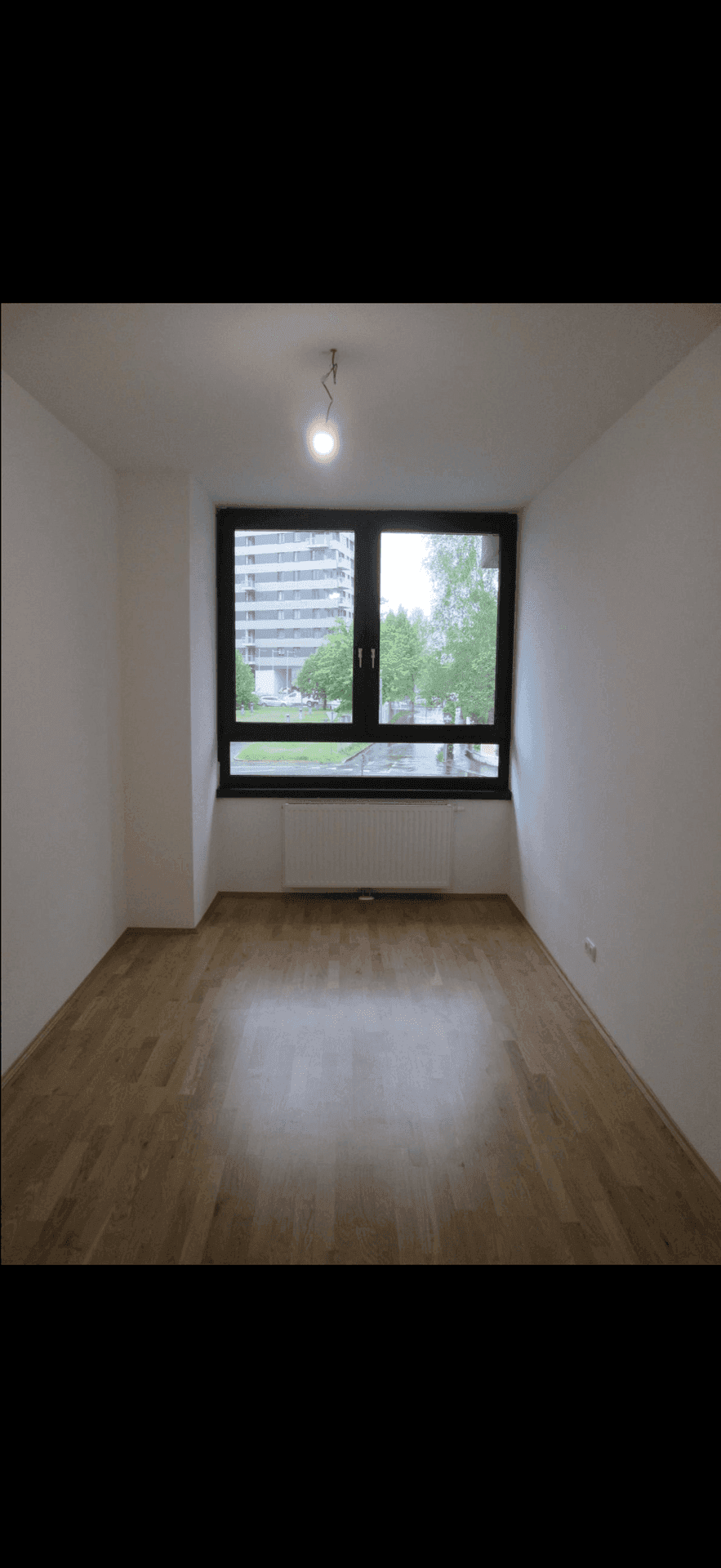 Leeres Zimmer mit Holzboden und einem großen Fenster, das viel Tageslicht hereinlässt.