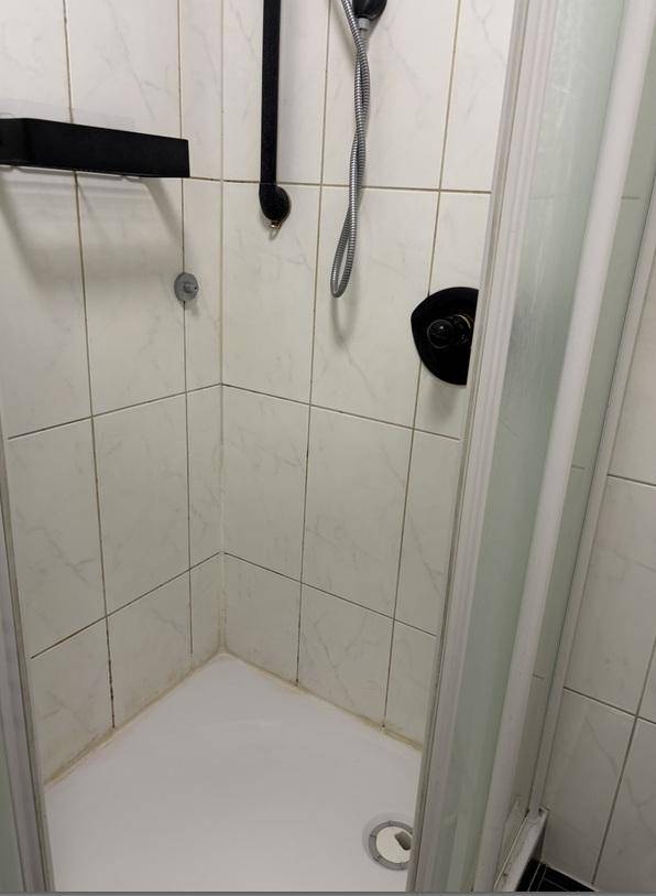 Duschkabine mit weißen Fliesen und schwarzer Armatur in einem Badezimmer.