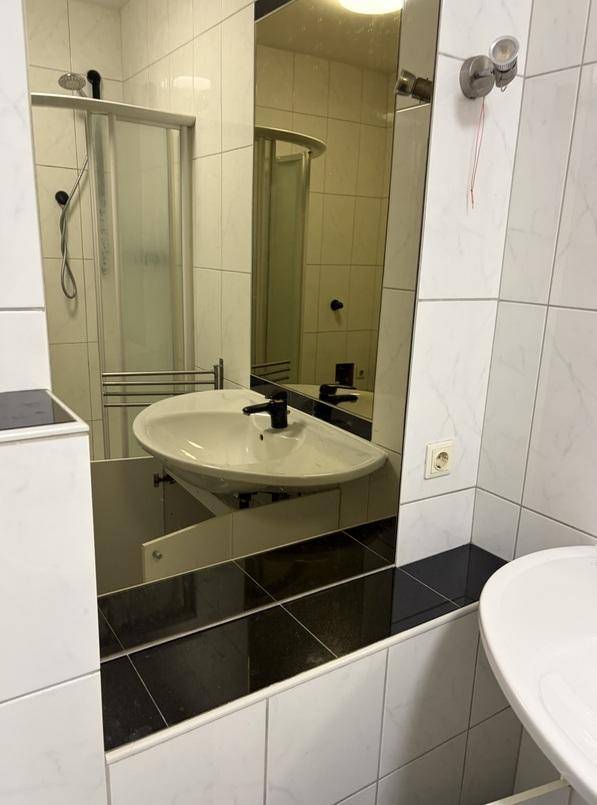 Badezimmer mit Waschbecken, großem Spiegel und weißen sowie schwarzen Fliesen.