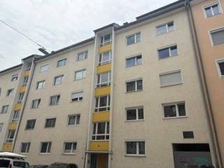 Mehrfamilienhaus mit heller Fassade, vielen Fenstern und gelben Akzenten an den Balkonen.