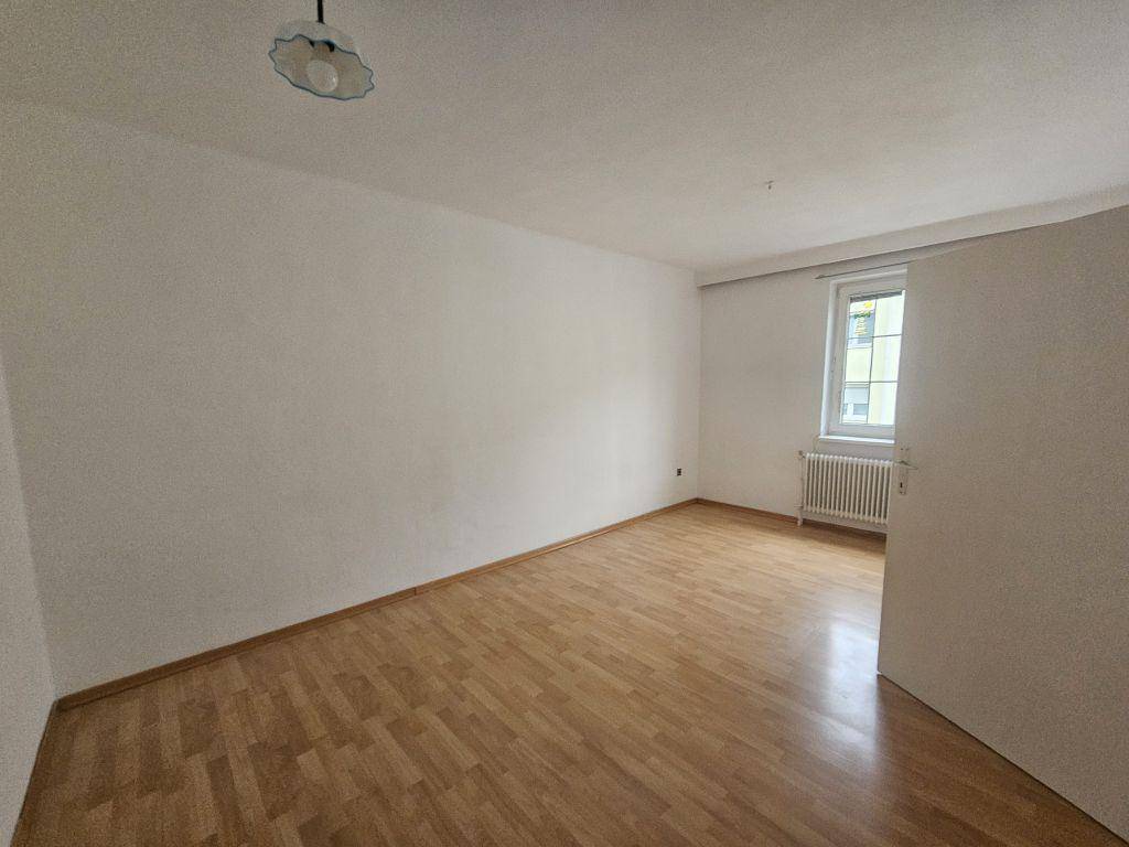 Helles Zimmer mit Laminatboden, weißen Wänden und einem Fenster, das Tageslicht hereinlässt.