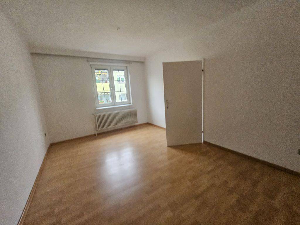 Leeres Schlafzimmer mit Laminatboden, weißen Wänden und einem Fenster mit Heizkörper.
