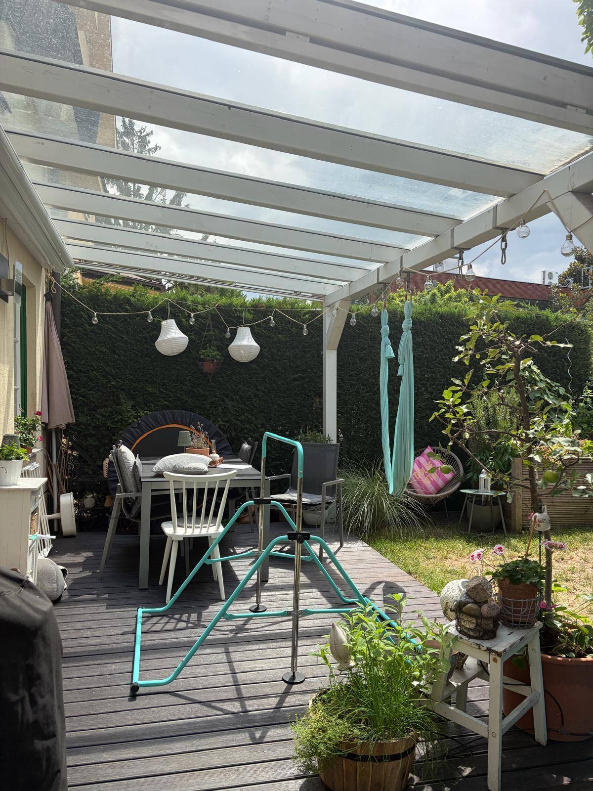 Überdachte Terrasse mit Esstisch, einem Pizzaofen und üppiger Bepflanzung.
