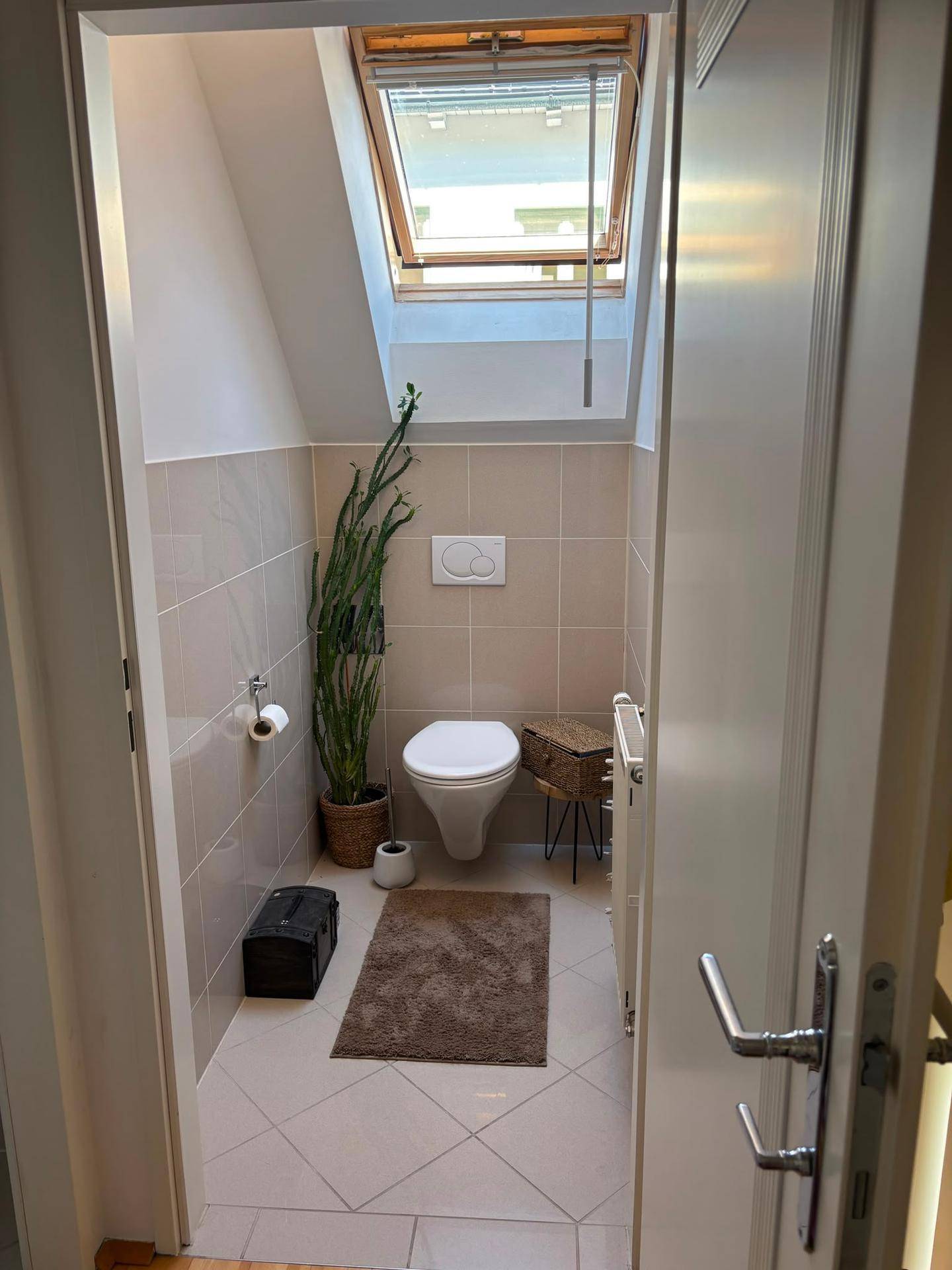 Gäste-WC mit wandhängender Toilette, Fliesen und einem Dachfenster für natürliches Licht.