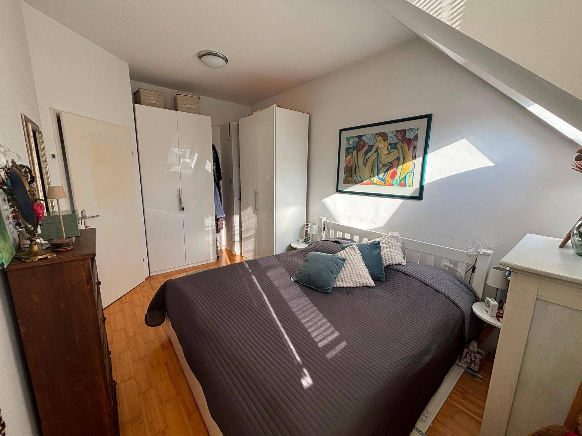 Schlafzimmer mit Doppelbett, weißen Kleiderschränken und Dachschräge mit Dachfenster.