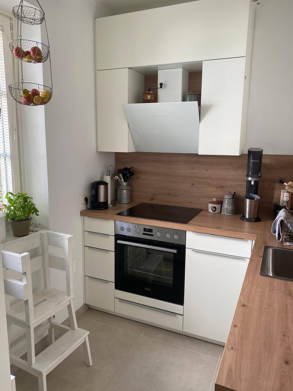 Moderne Küche mit weißen Schränken, Holzarbeitsplatten und integrierten Elektrogeräten.
