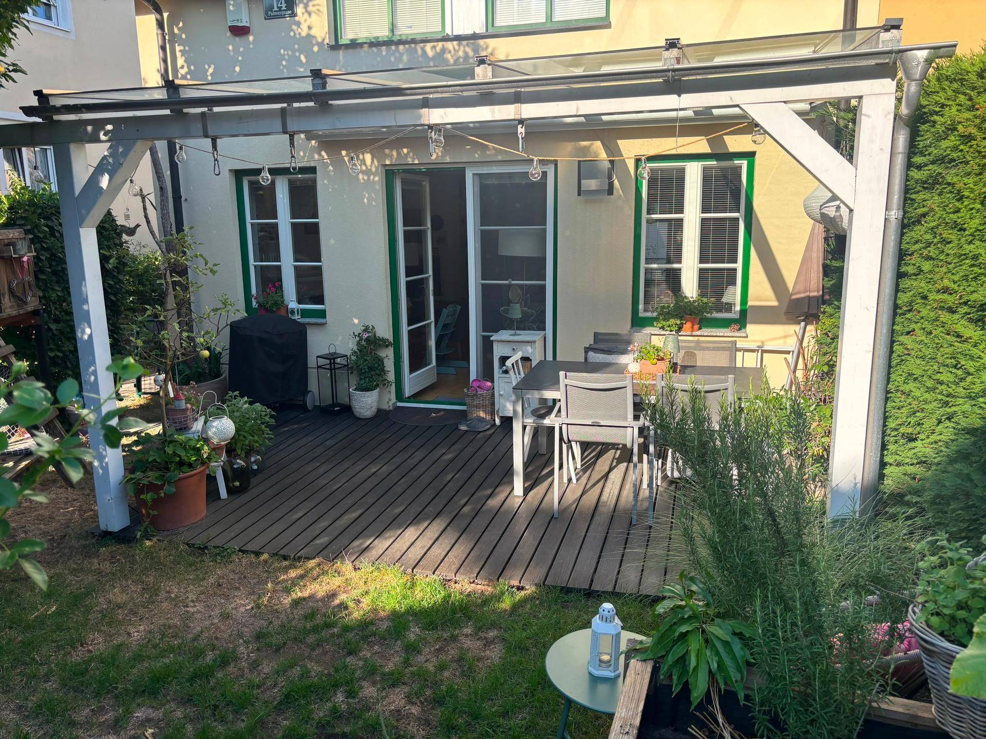 Überdachte Holzterrasse mit Gartenmöbeln und Zugang zu einem kleinen Rasenbereich.
