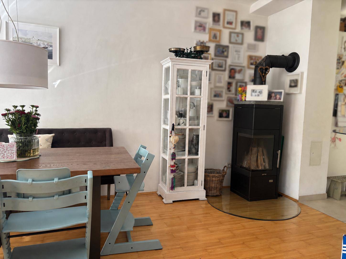 Essbereich mit Holztisch, Vitrine und einem modernen Holzofen, der für Wärme sorgt.