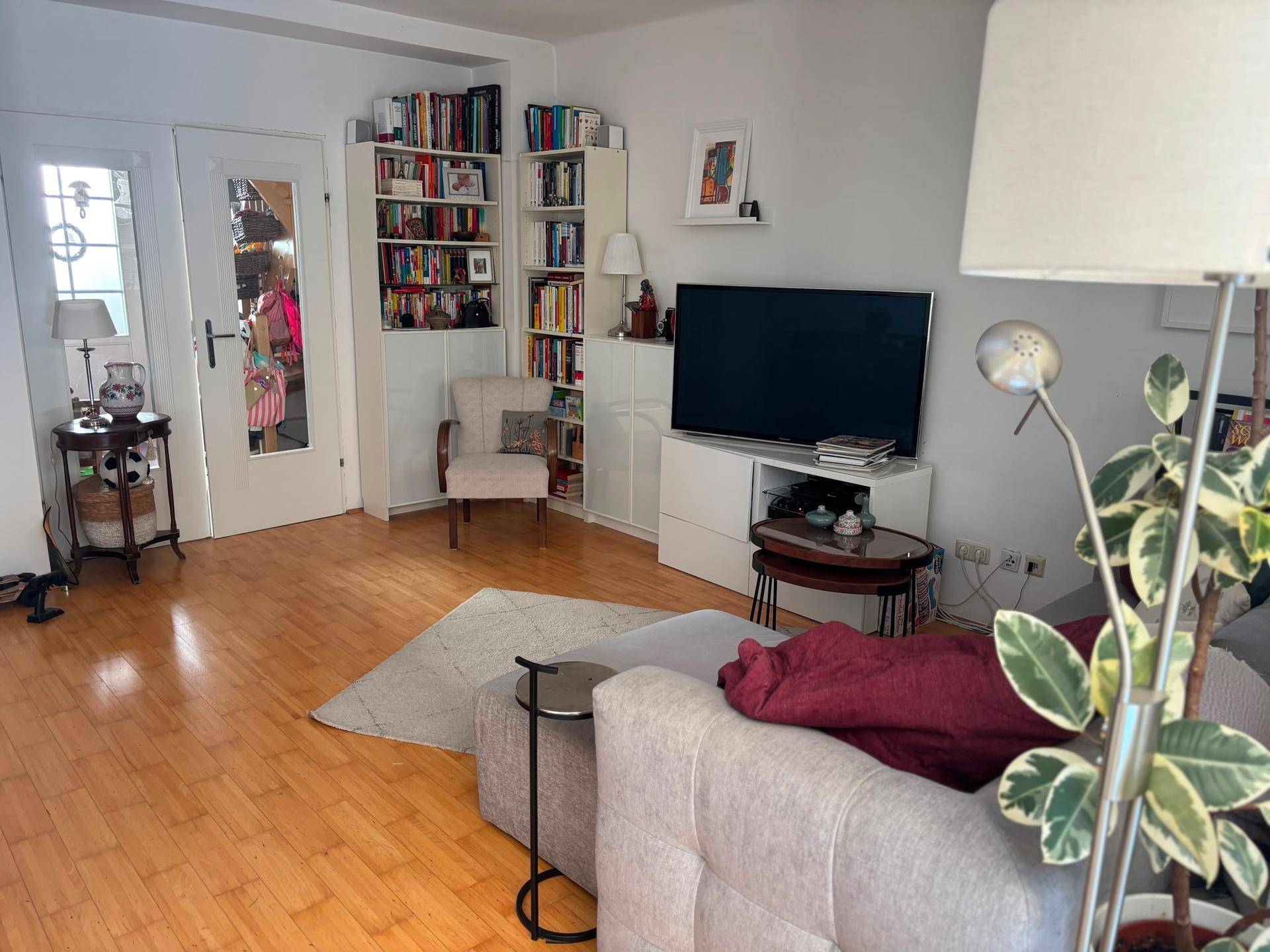 Gemütliches Wohnzimmer mit Bücherregalen, einem bequemen Sessel und hellem Holzfußboden.