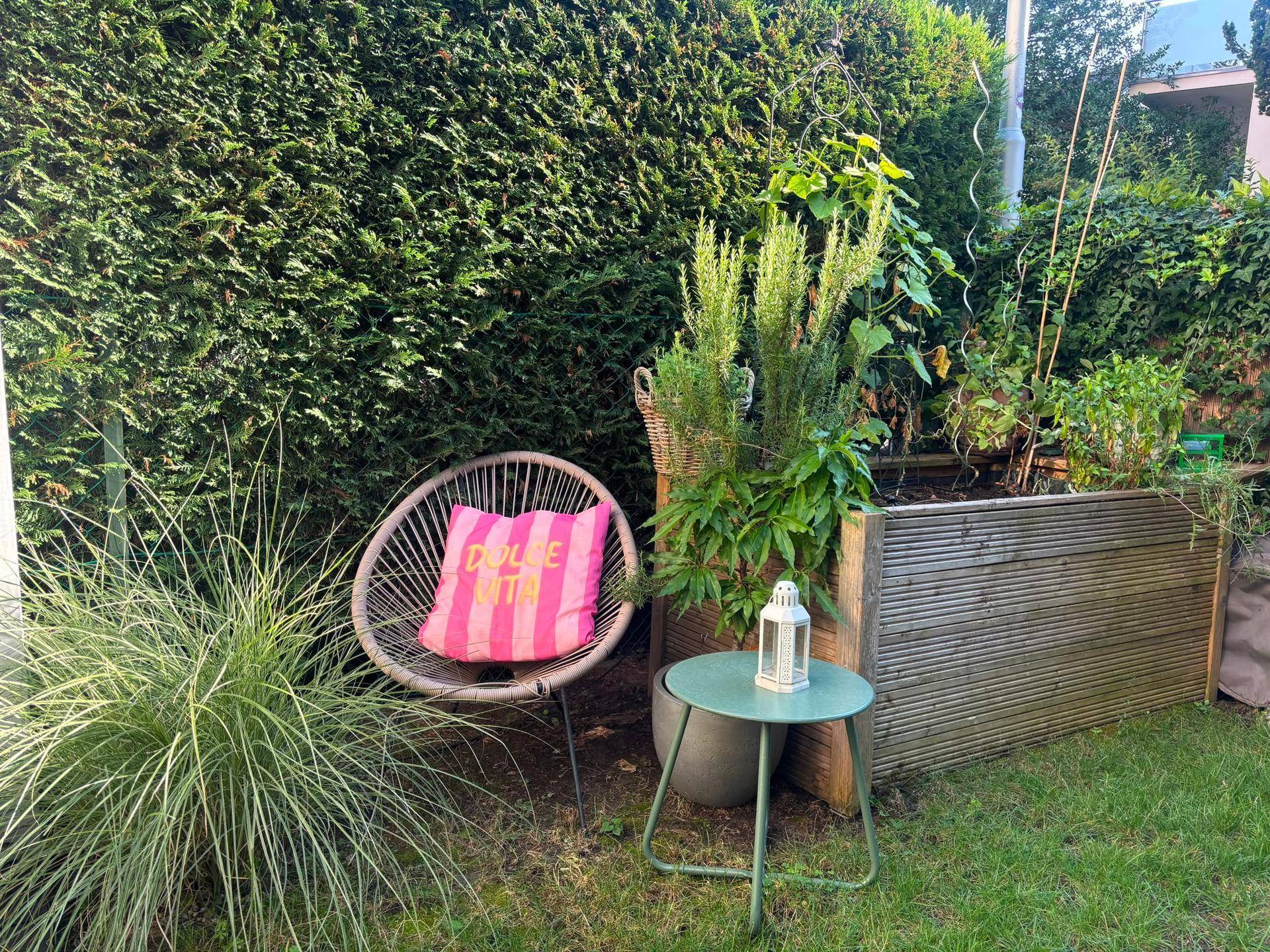 Gemütlicher Gartenbereich mit Sitzgelegenheit, Beistelltisch und Hochbeeten für Pflanzen.