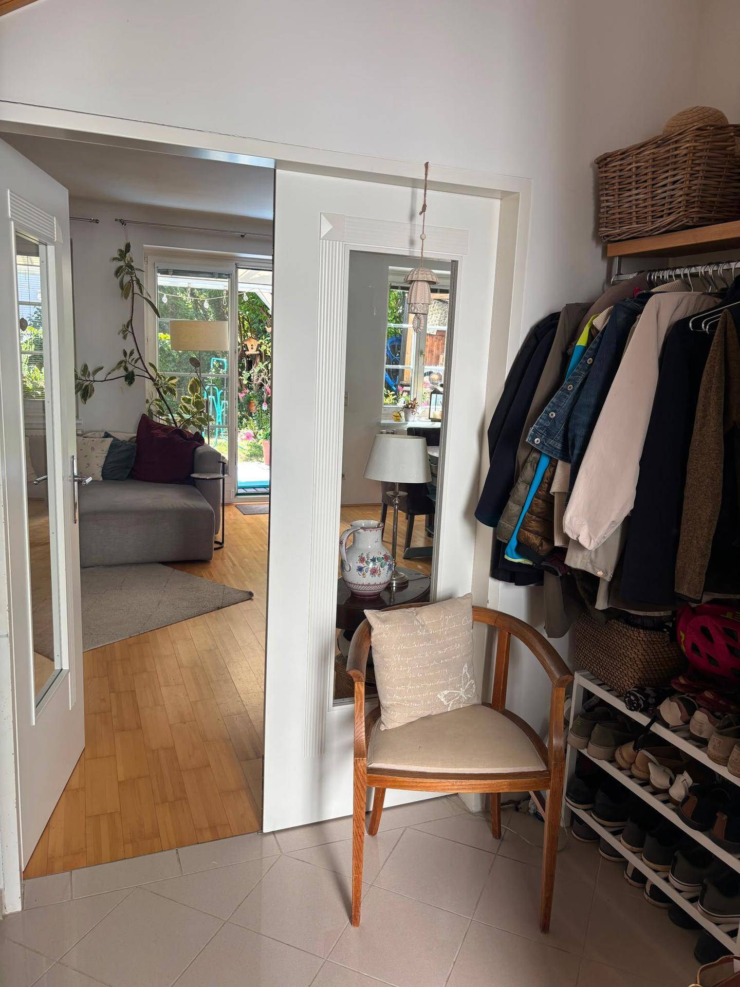 Eingangsbereich mit Garderobe und Schuhregal, der in ein helles Wohnzimmer führt.