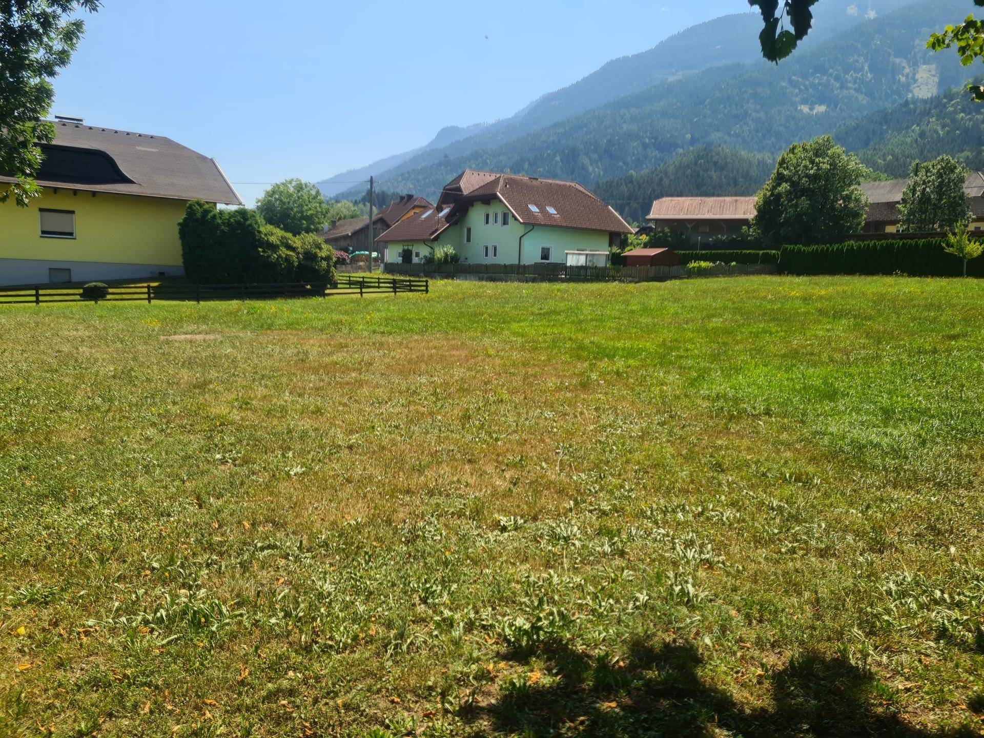 Panoramablick über eine Wiese mit Wohnhäusern und einer beeindruckenden Bergkulisse.