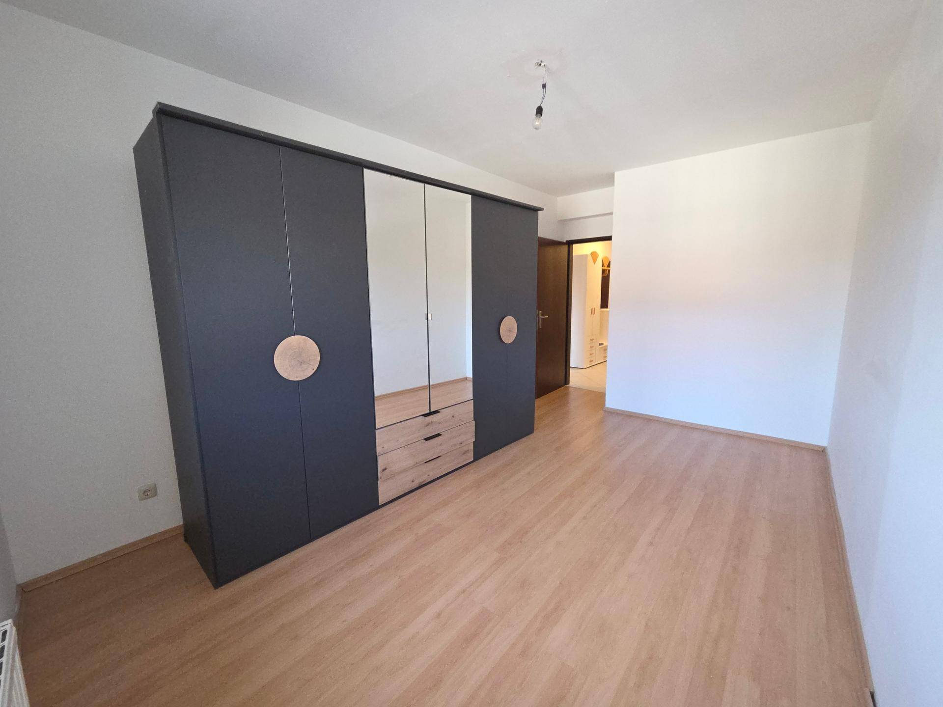 Geräumiges Schlafzimmer mit Laminatboden und einem großen modernen Kleiderschrank mit Spiegeltüren.