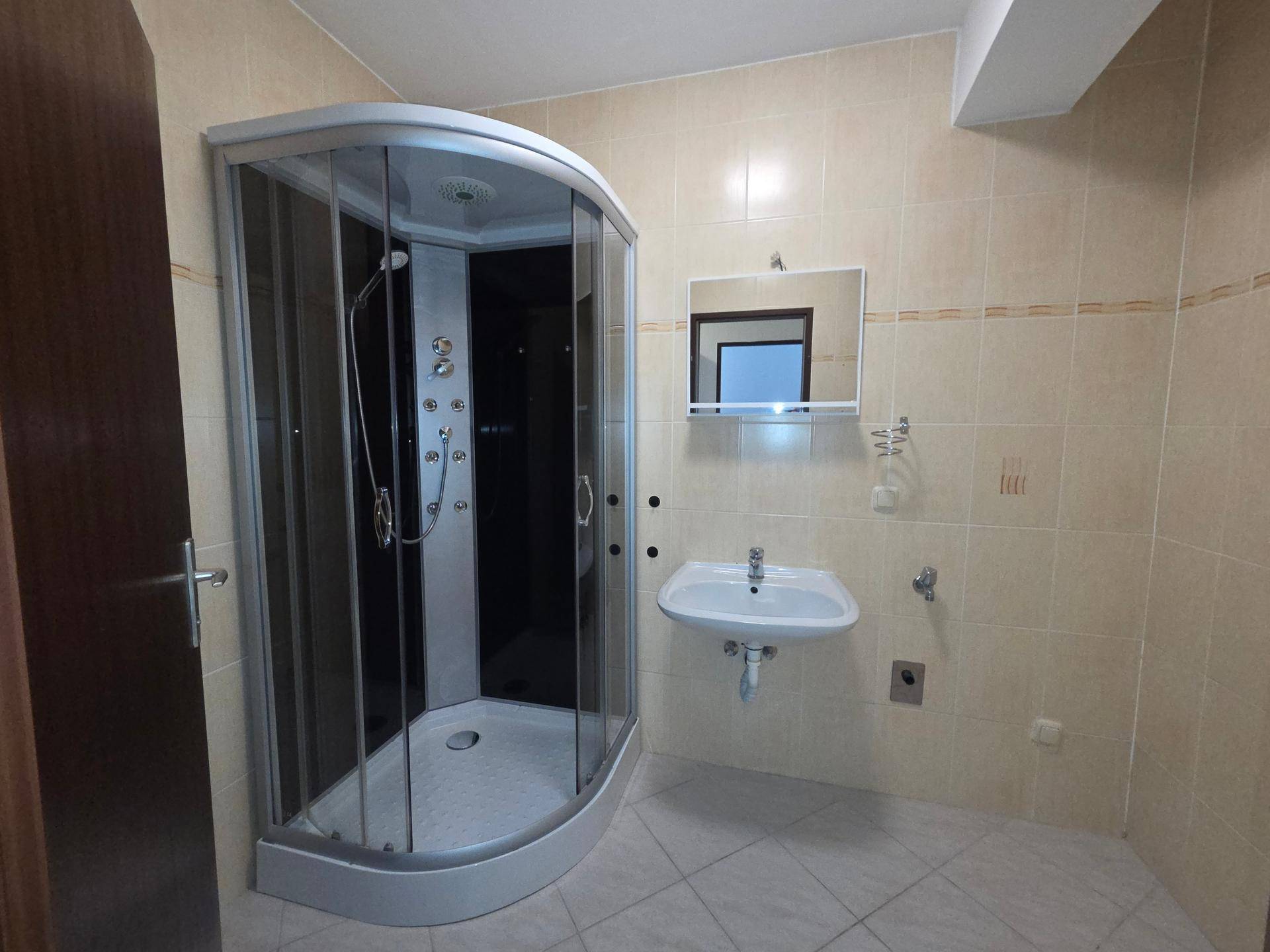 Badezimmer mit beigefarbenen Fliesen, einer modernen Duschkabine und einem einzelnen Waschbecken.