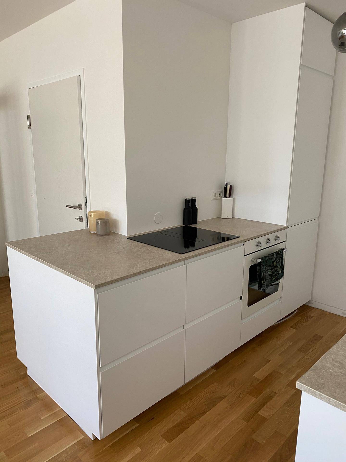 Detailansicht der modernen Küche mit Induktionskochfeld, Backofen und weißen Unterschränken.