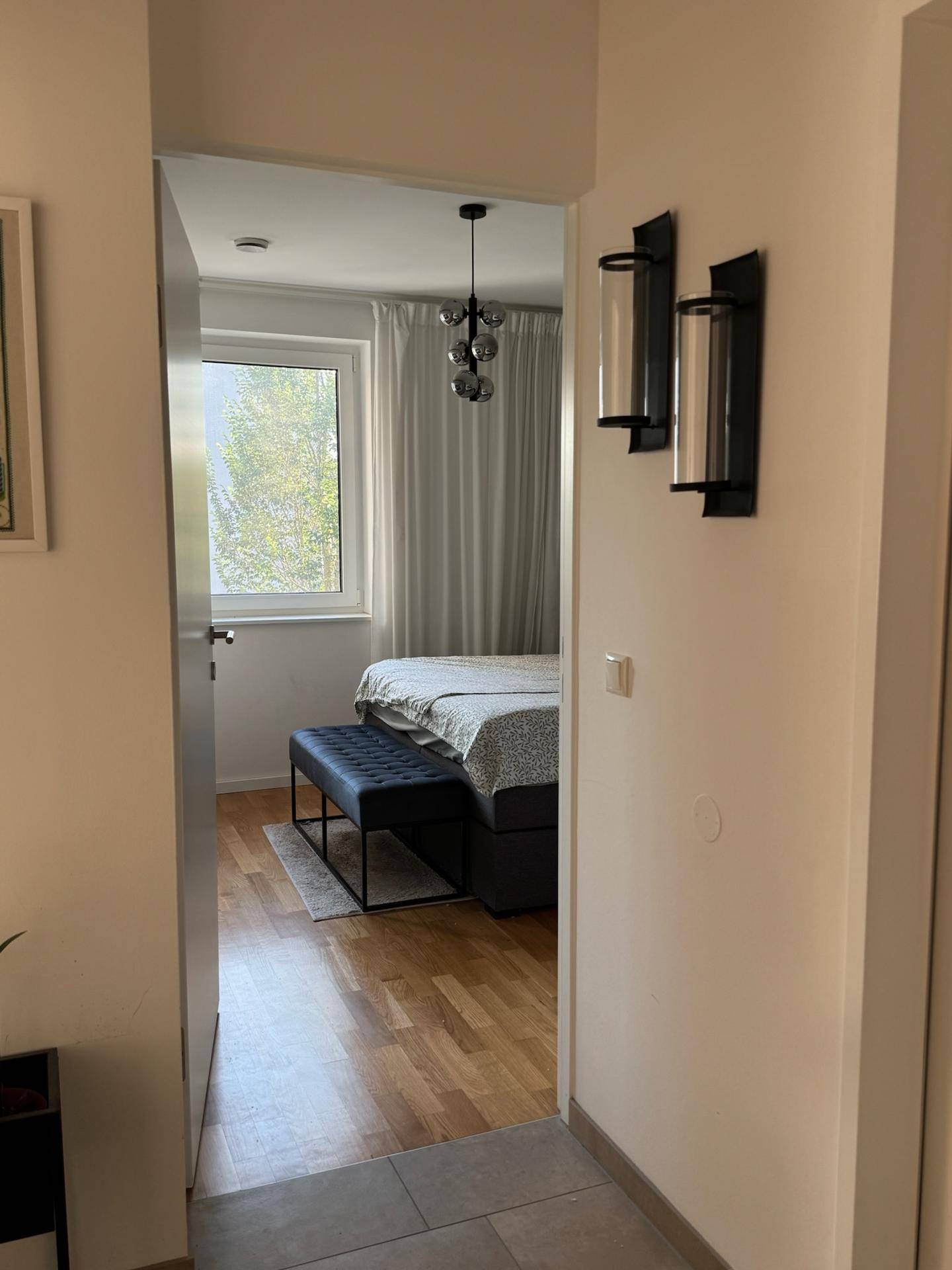 Blick in ein helles Schlafzimmer mit Holzboden und großem Fenster.