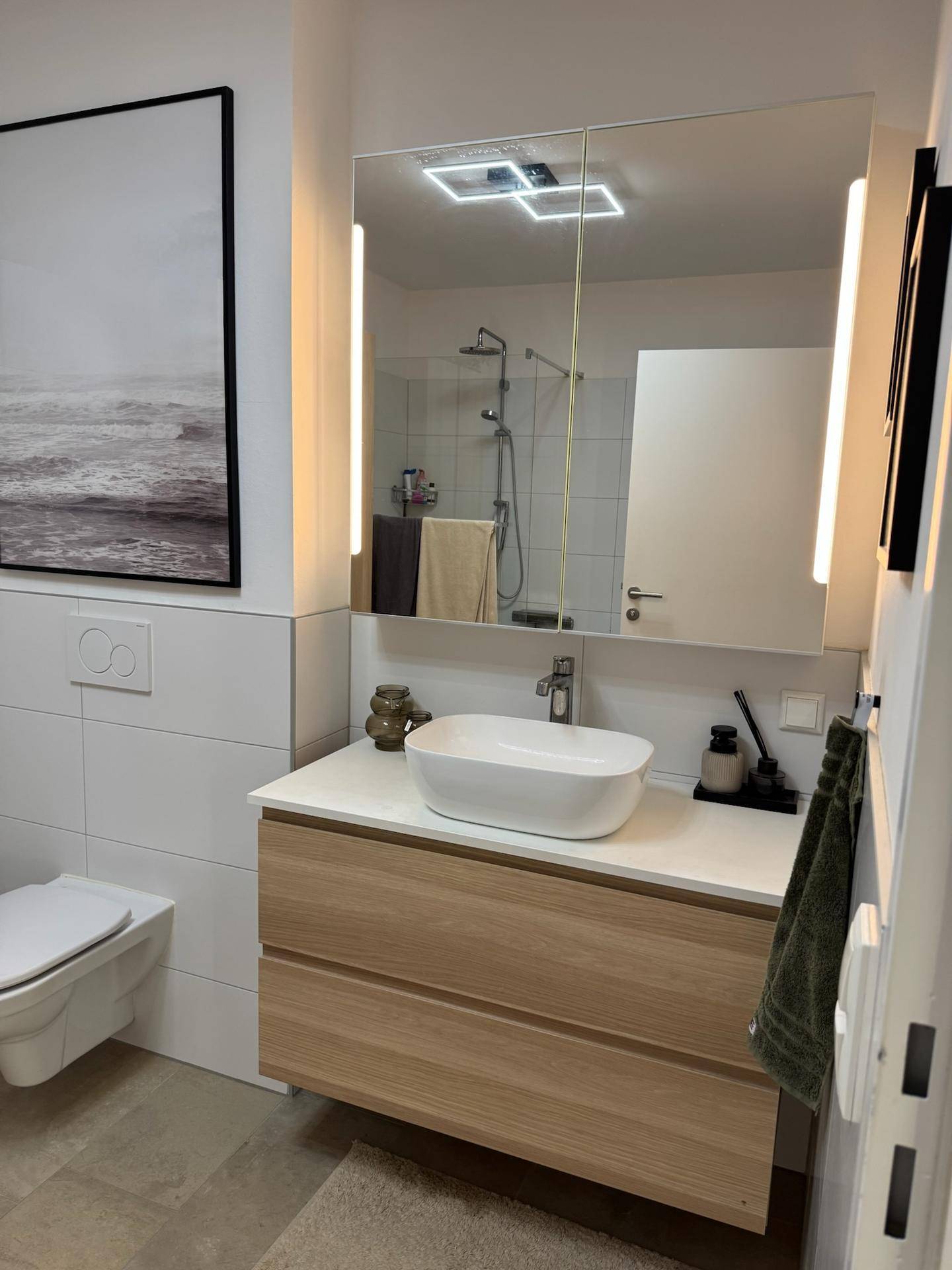 Modernes Badezimmer mit Einzelwaschbecken, beleuchtetem Spiegelschrank und Wand-WC.