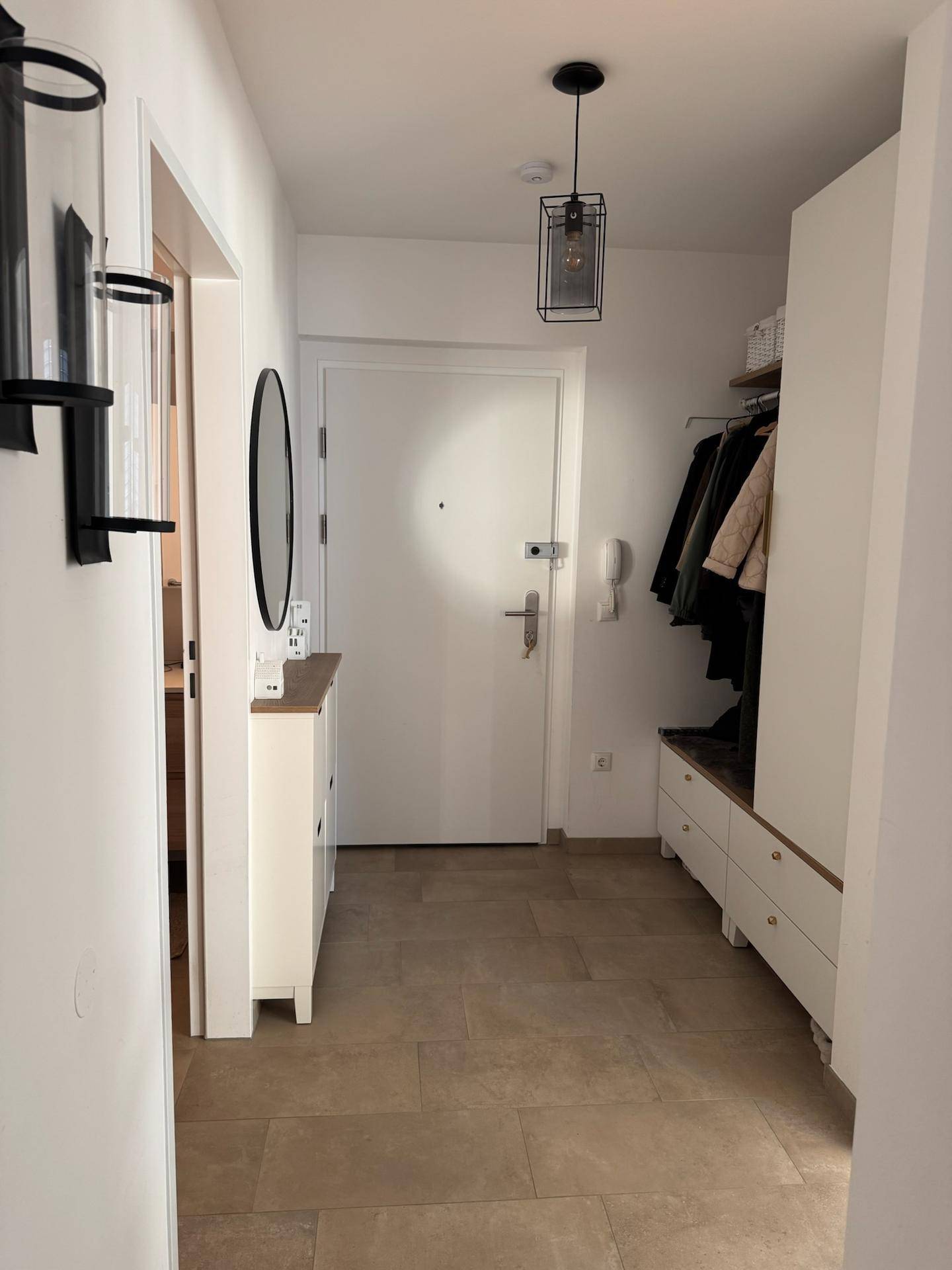 Heller Eingangsbereich mit beigefarbenen Fliesen, Garderobe und modernem Deckenlicht.