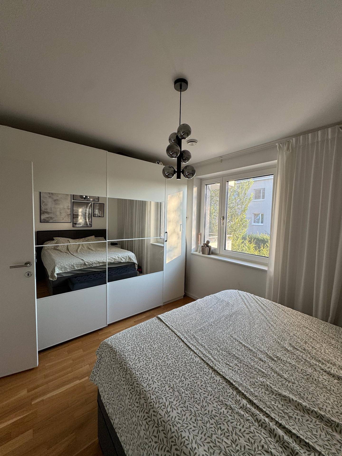 Modernes Schlafzimmer mit großem Bett, Spiegelschrank und viel Tageslicht.