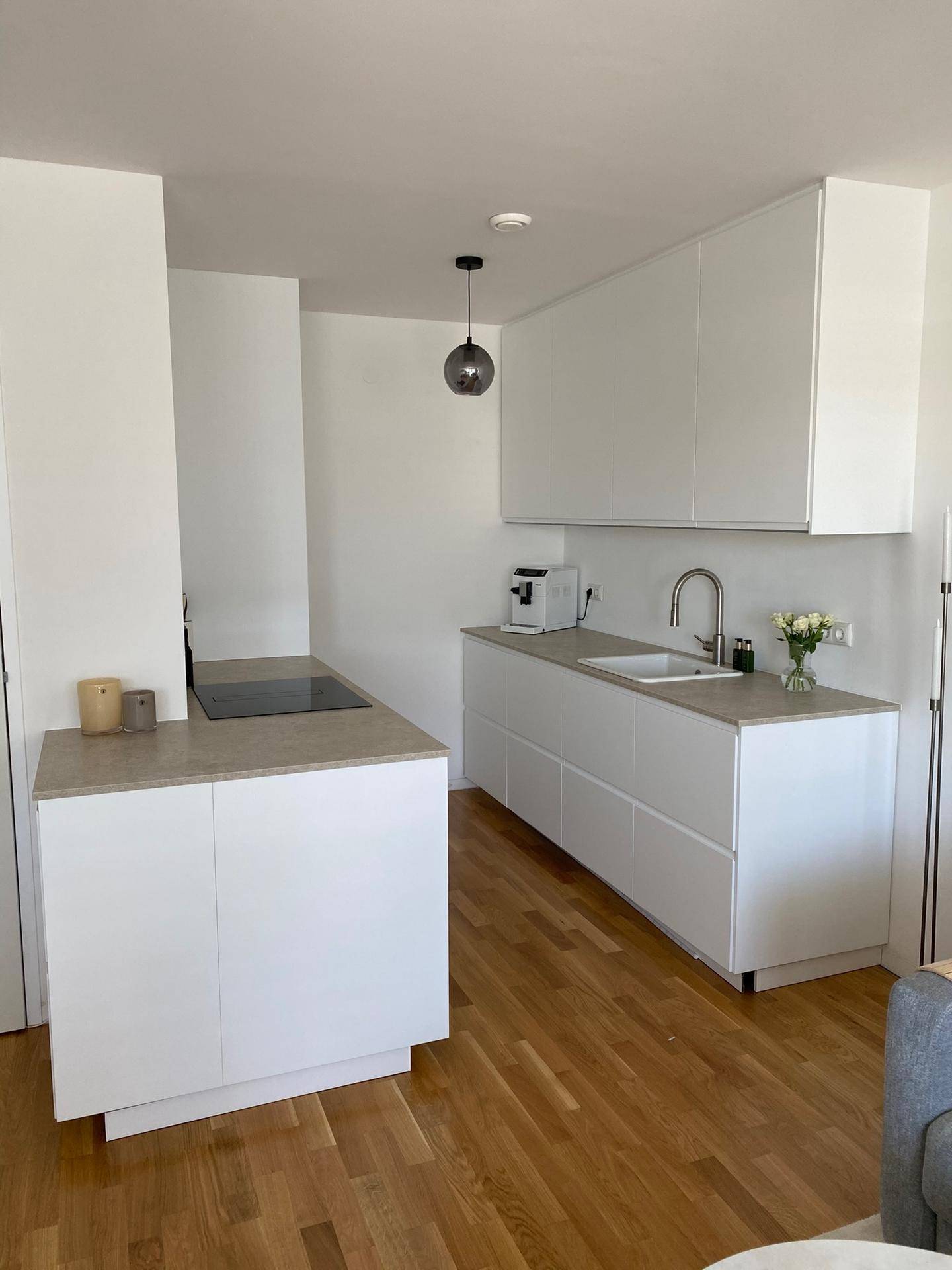 Moderne, offene Küche mit weißen Schränken, heller Arbeitsplatte und integrierten Geräten.
