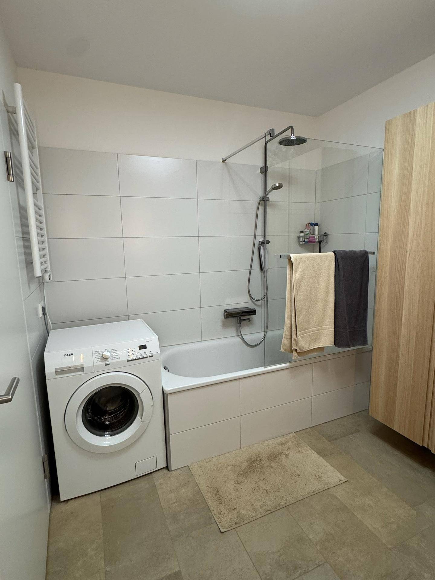 Badezimmer mit Badewanne, integrierter Duschfunktion und Waschmaschine.