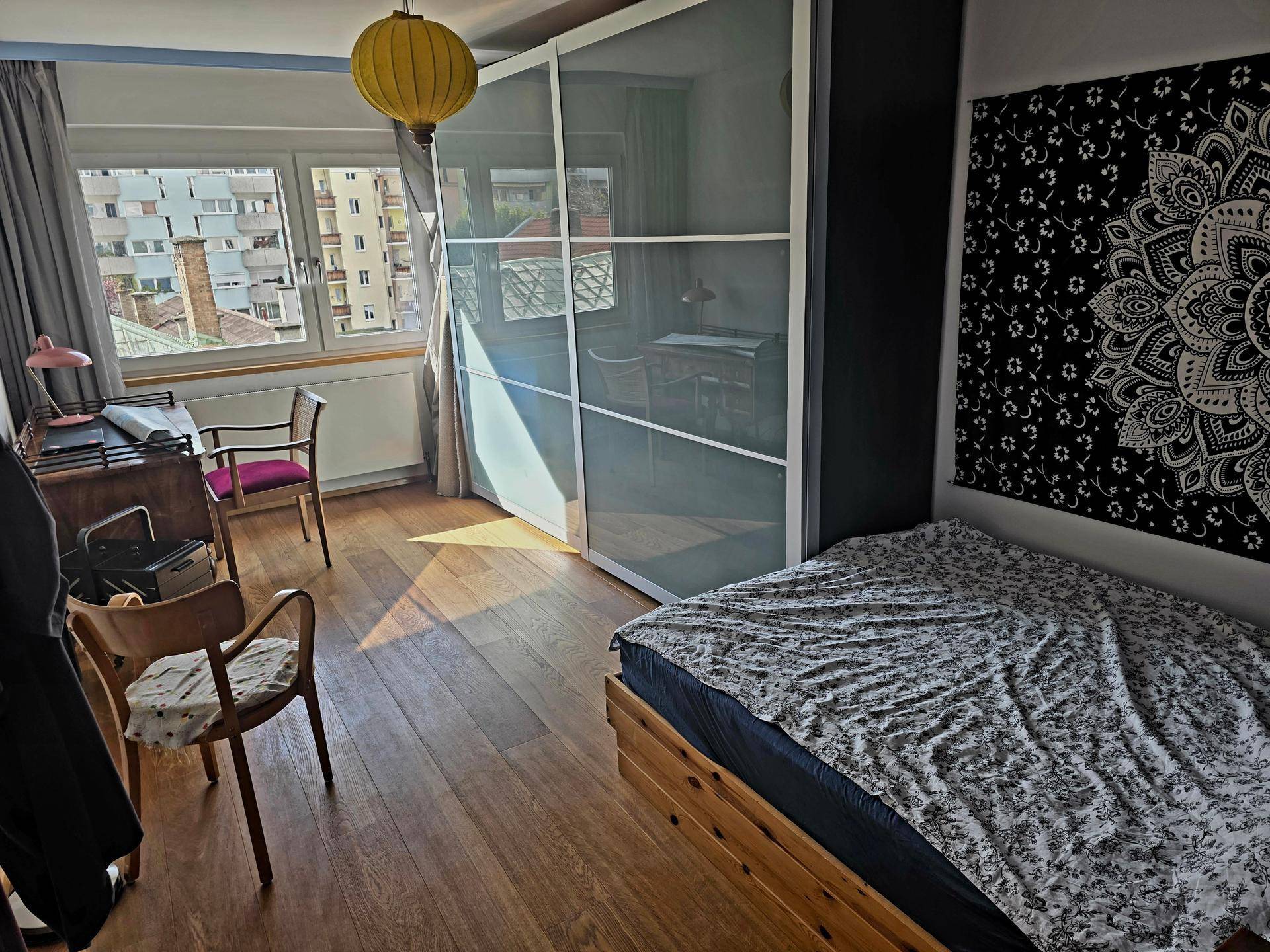 Schlafzimmer mit Holzboden, großem Kleiderschrank und Schreibtisch, bietet einen urbanen Ausblick.