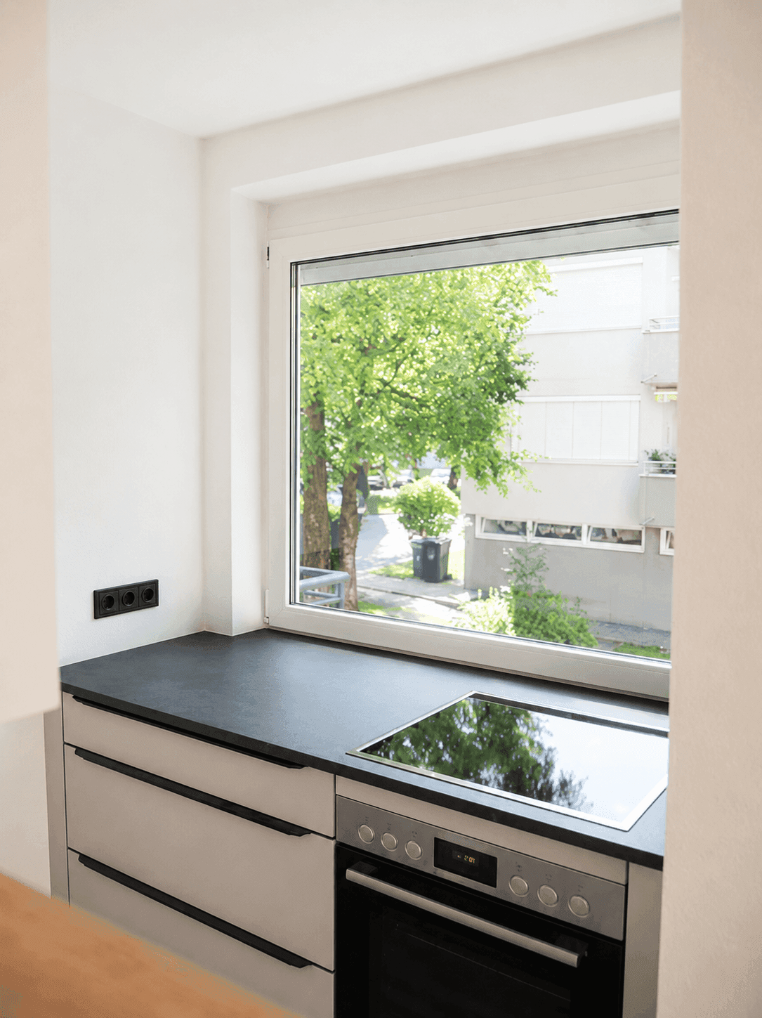 Küchenbereich mit Fenster und Blick ins Grüne, ausgestattet mit integriertem Backofen und Induktionskochfeld.