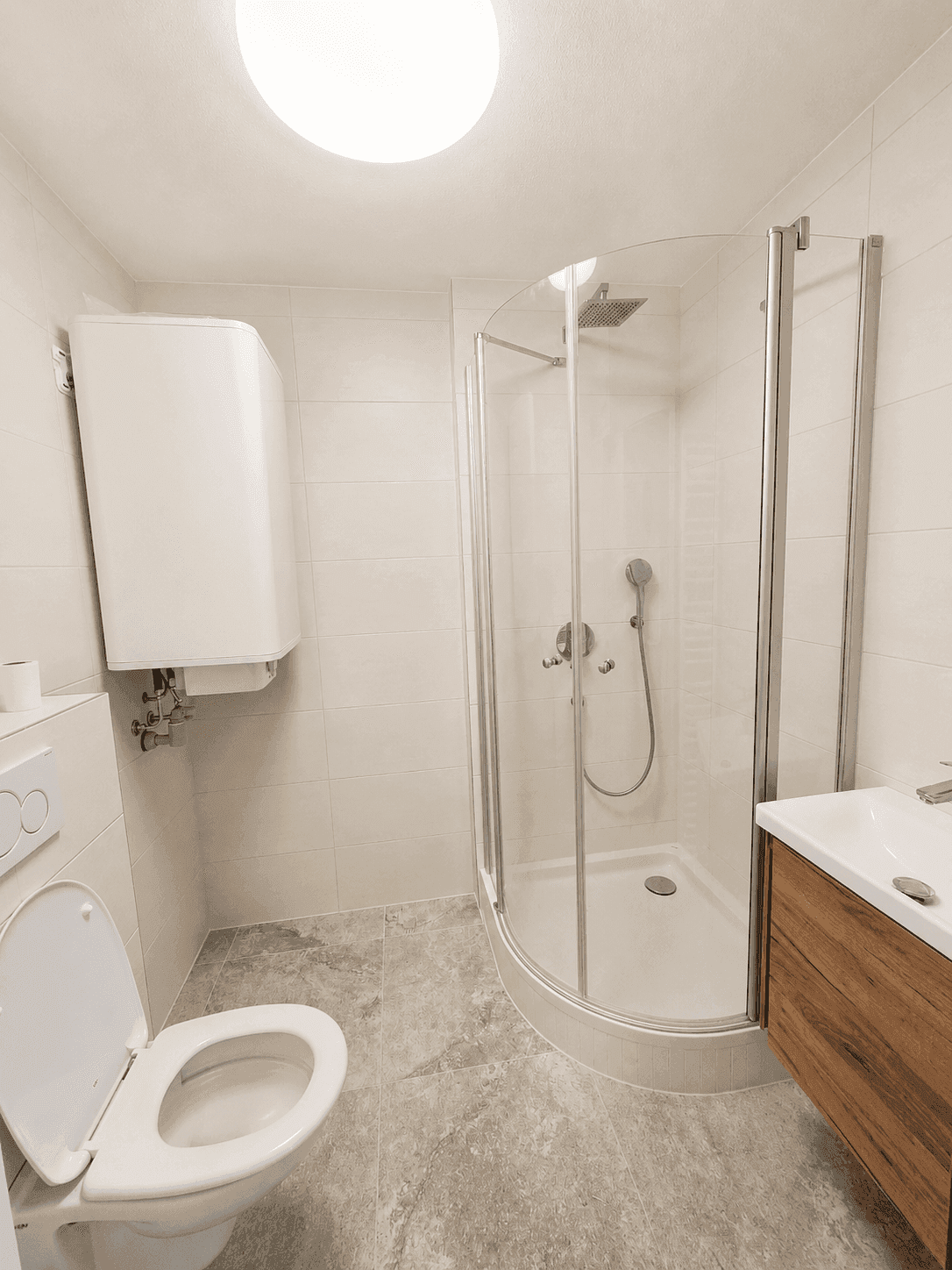 Modernes Badezimmer mit Duschkabine, WC und Holzwaschtisch, ausgestattet mit hellen Fliesen und Warmwasserboiler.