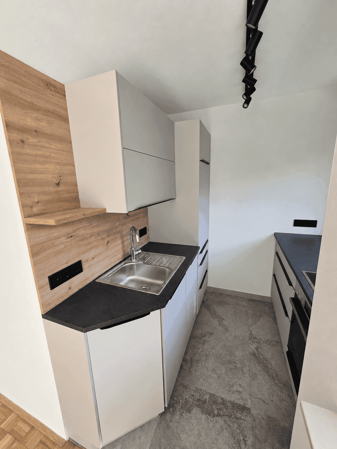 Moderne Einbauküche mit weißen Schränken, dunklen Arbeitsplatten und Holzrückwand, bietet eine funktionale Kochumgebung.