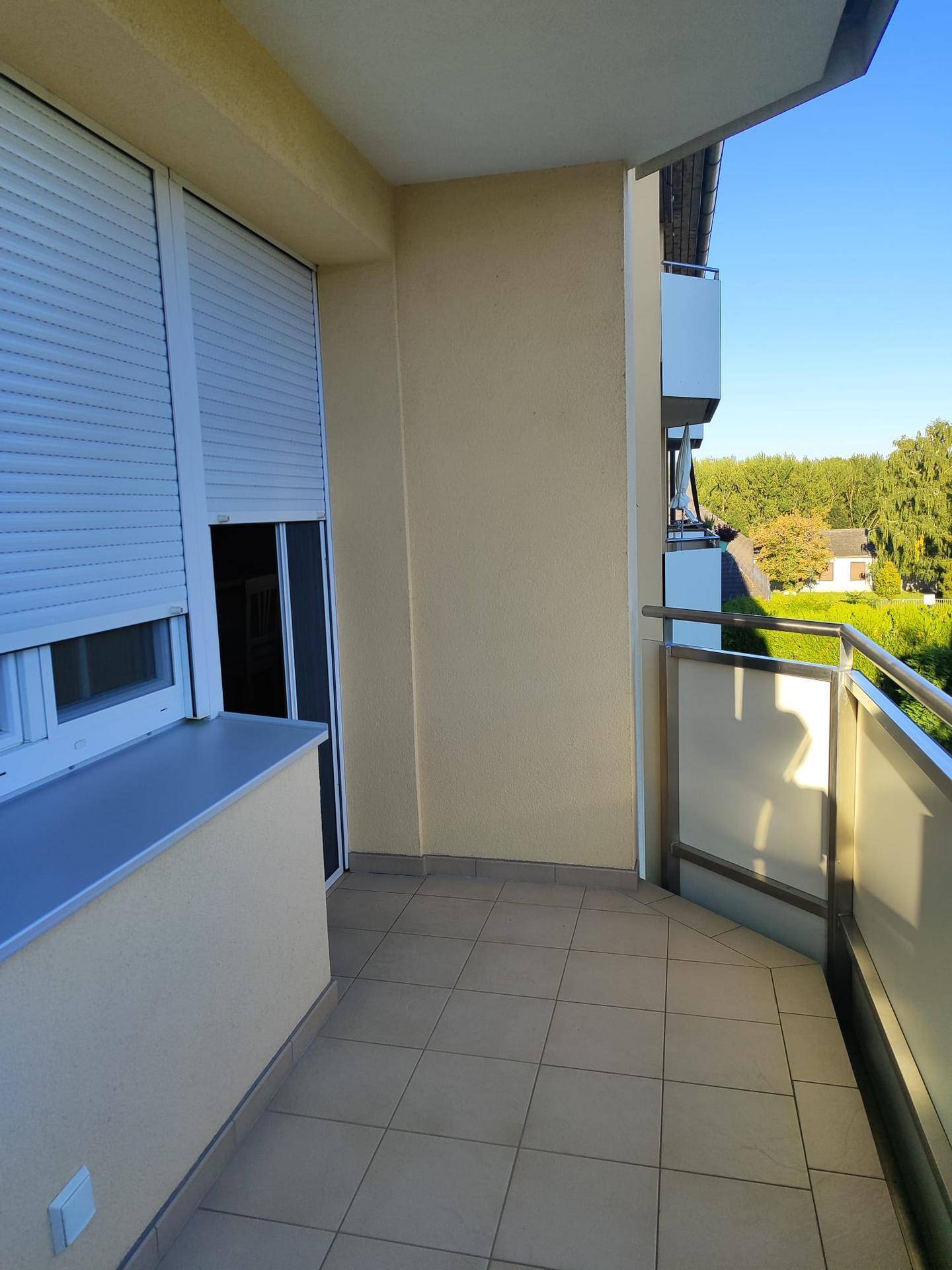 Heller Balkon mit Fliesenboden, moderner Brüstung und Blick ins Grüne.