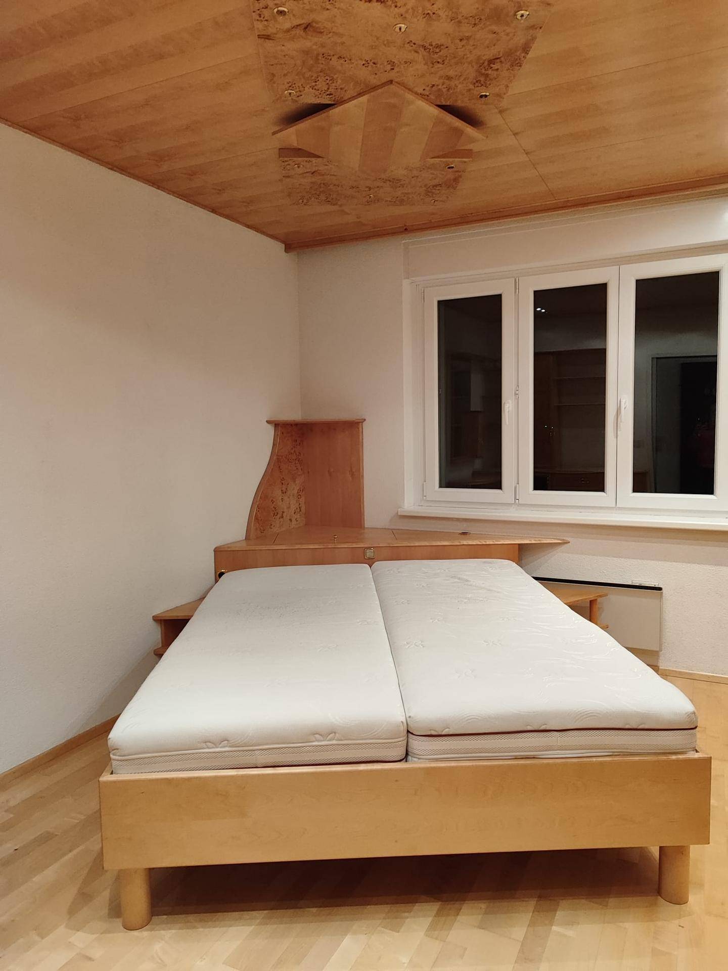 Helles Schlafzimmer mit Doppelbett, Holzdecke und Fenster mit Blick nach draußen.