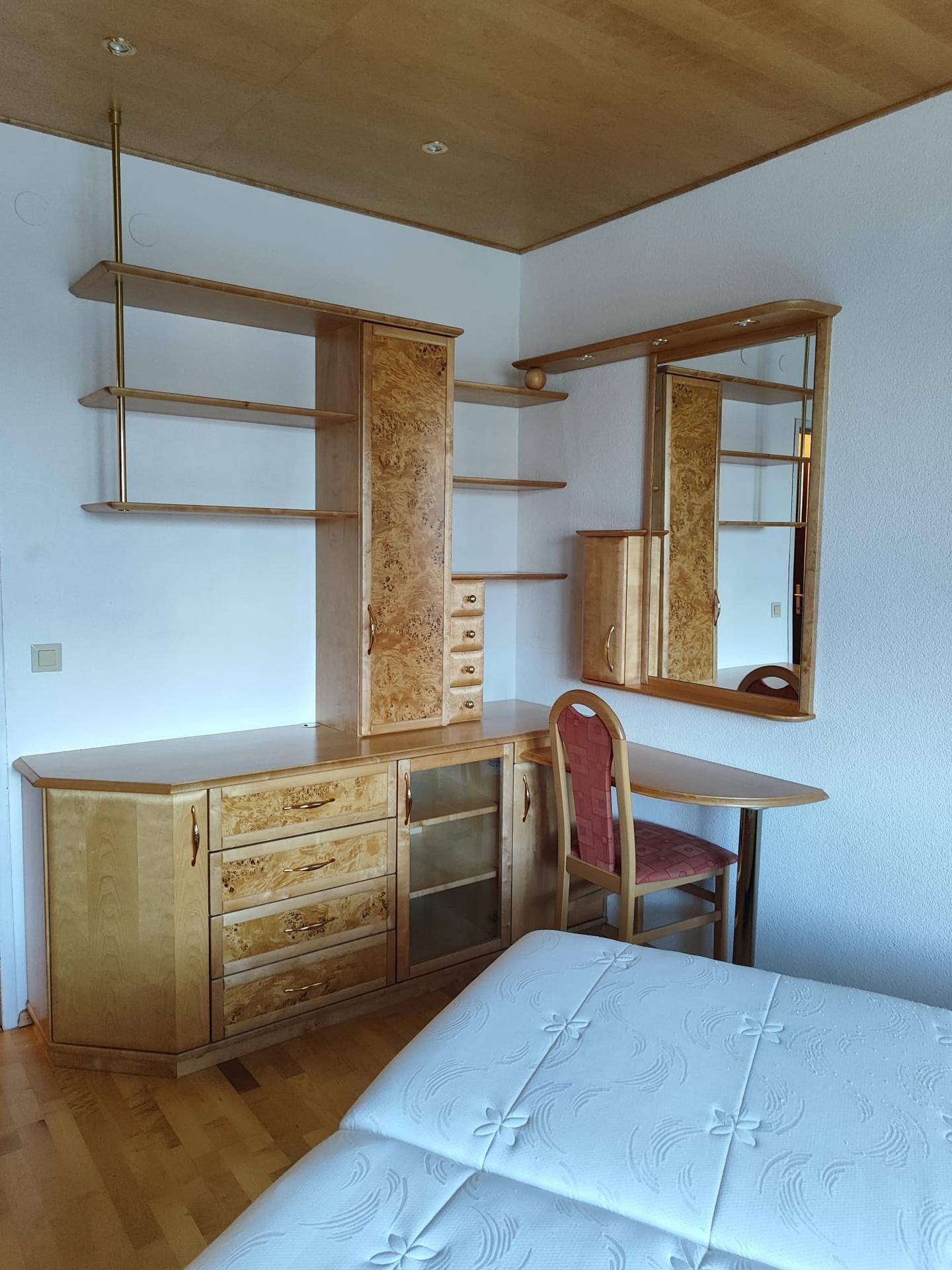 Schlafzimmer mit hellem Holzmobiliar, Regalen, Spiegel und integriertem Schreibtisch.