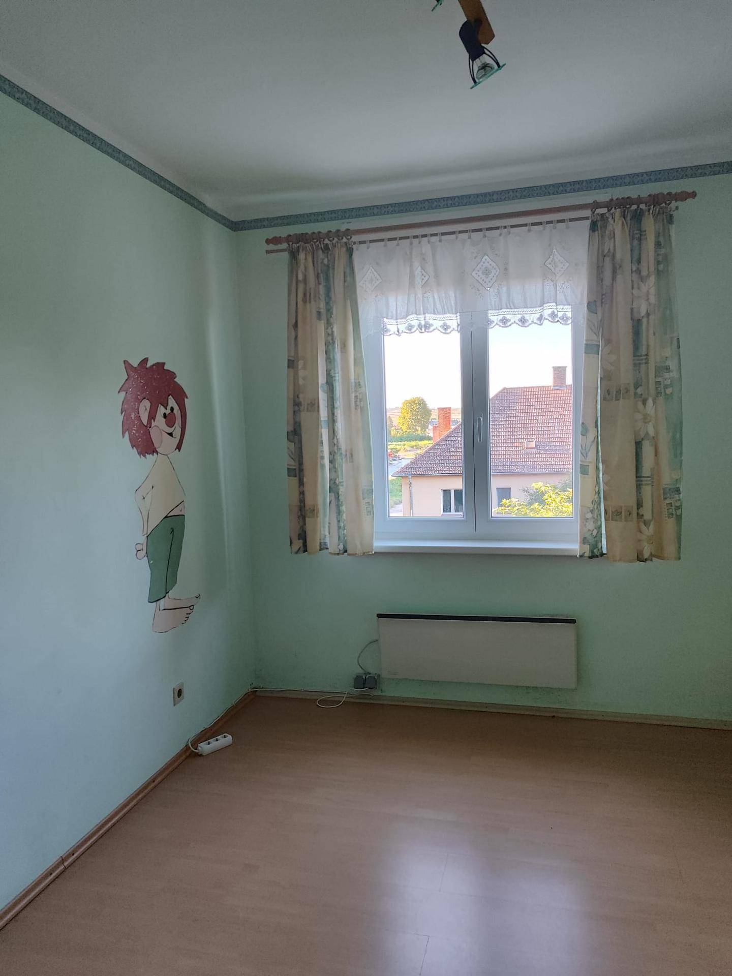 Kinderzimmer mit hellgrünen Wänden, Laminatboden und Fenster mit Ausblick.