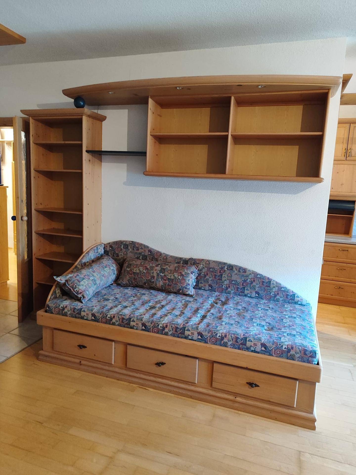 Wohnbereich mit bequemer Tagesliege, Holzregalen und hellem Holzfußboden.