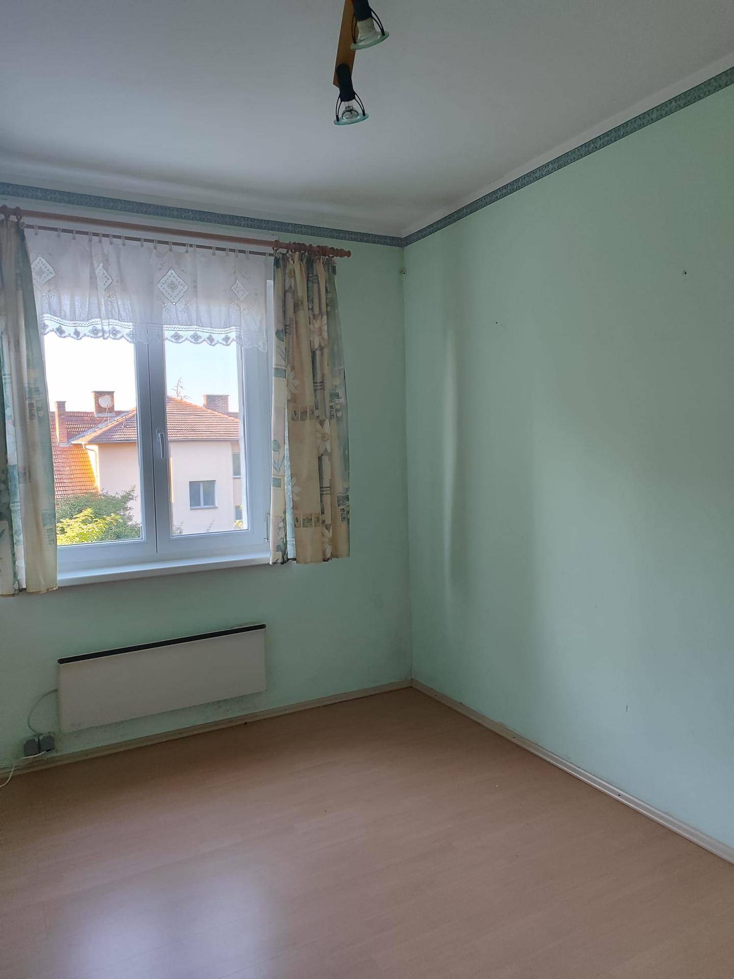 Helles Zimmer mit hellgrünen Wänden, Laminatboden und Fensterblick.