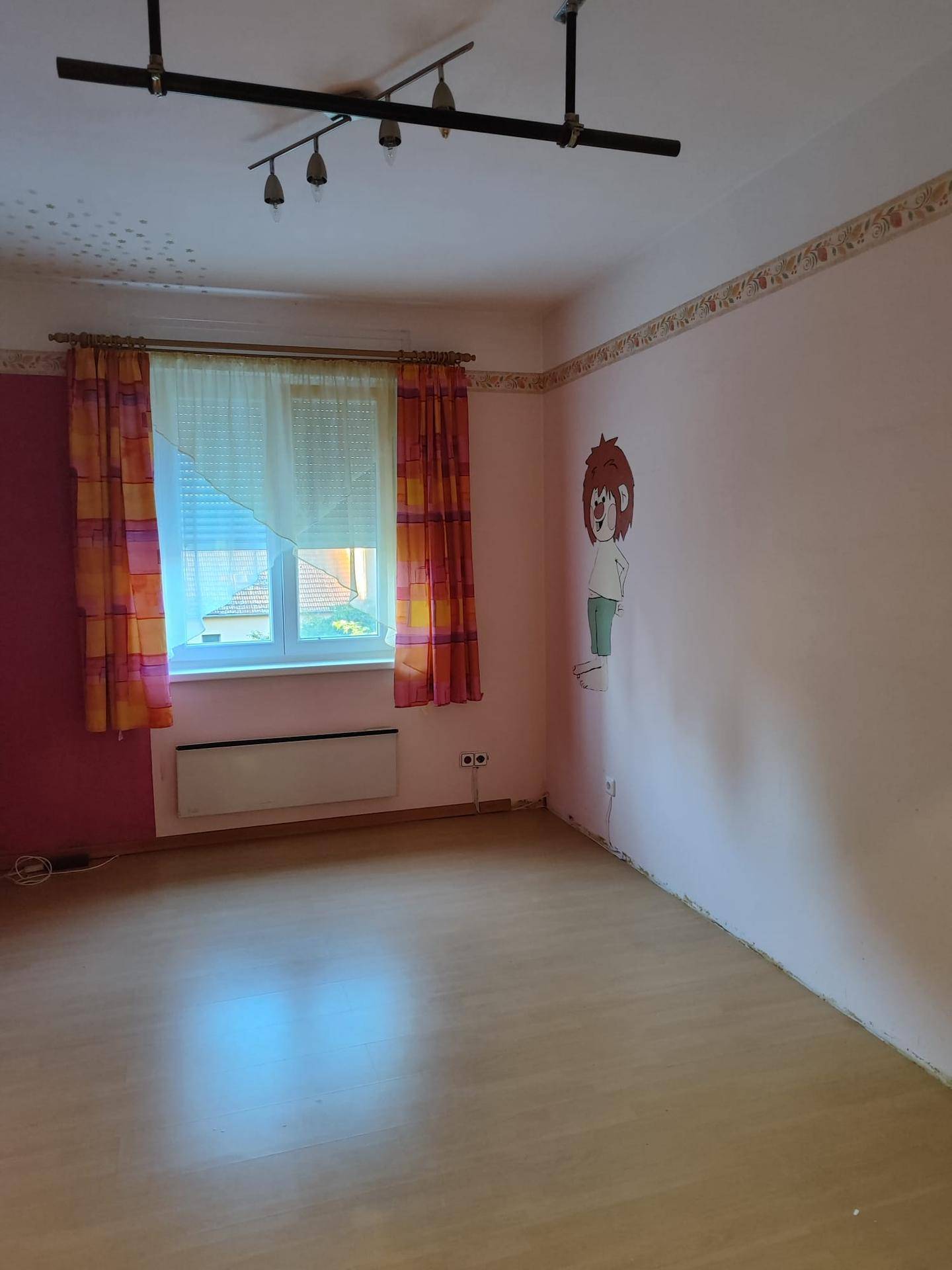 Helles Zimmer mit pinken Wänden, Laminatboden und Fenster mit Ausblick.
