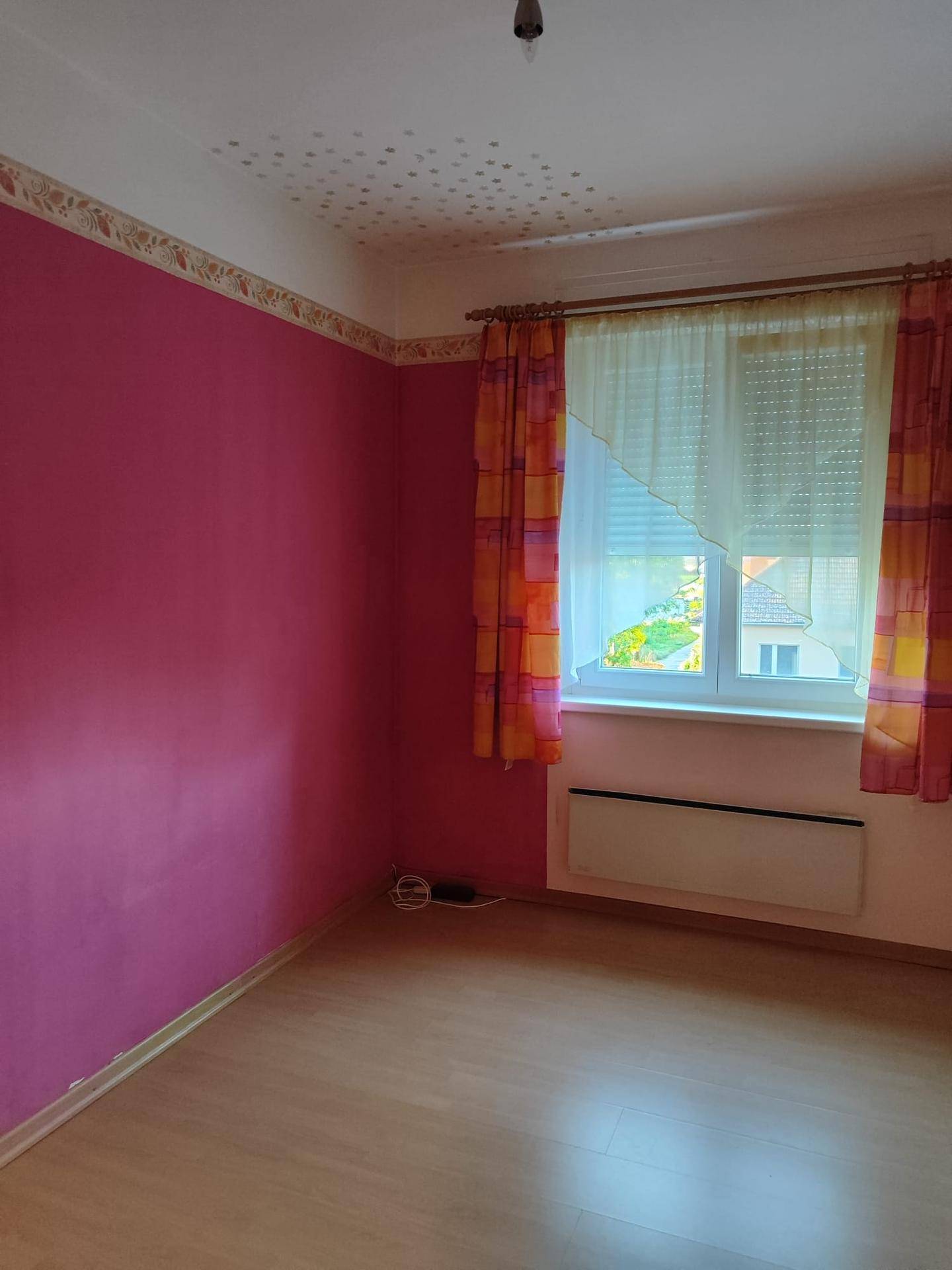 Zimmer mit leuchtend pinken Wänden, Laminatboden und Fenster mit Vorhängen.