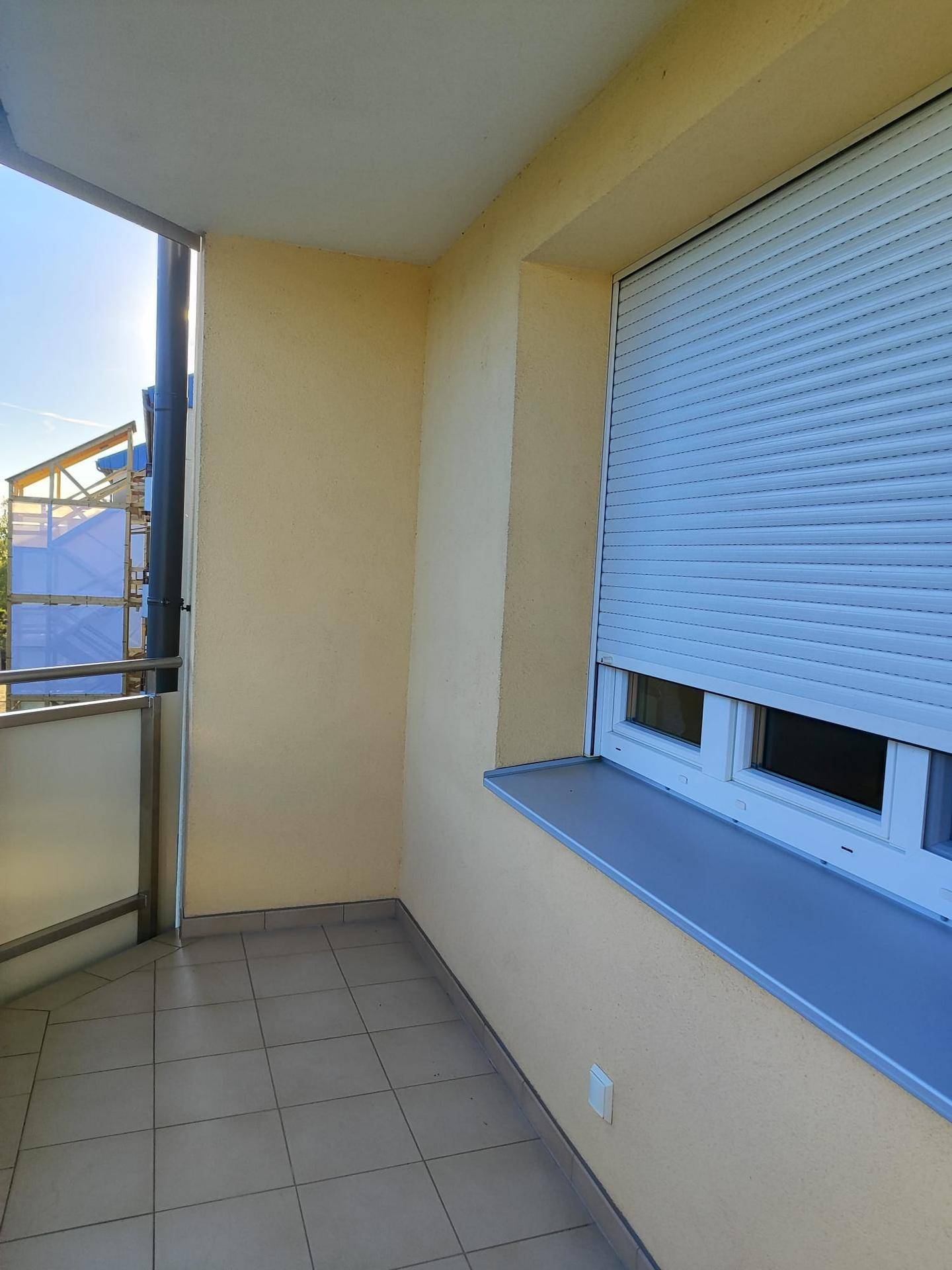 Sonniger Balkon mit Fliesenboden und Rollladen am Fenster, ideal für Entspannung.