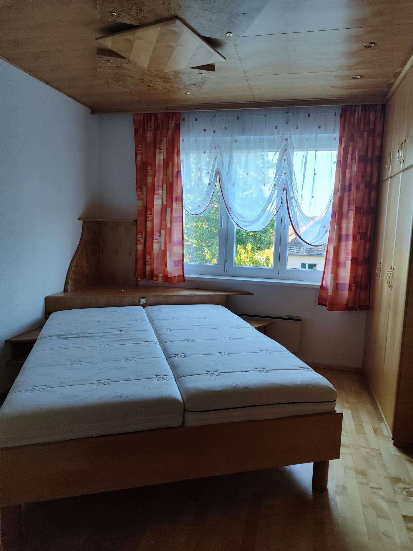 Helles Schlafzimmer mit Doppelbett, Holzdecke und Fenster mit Blick nach draußen.