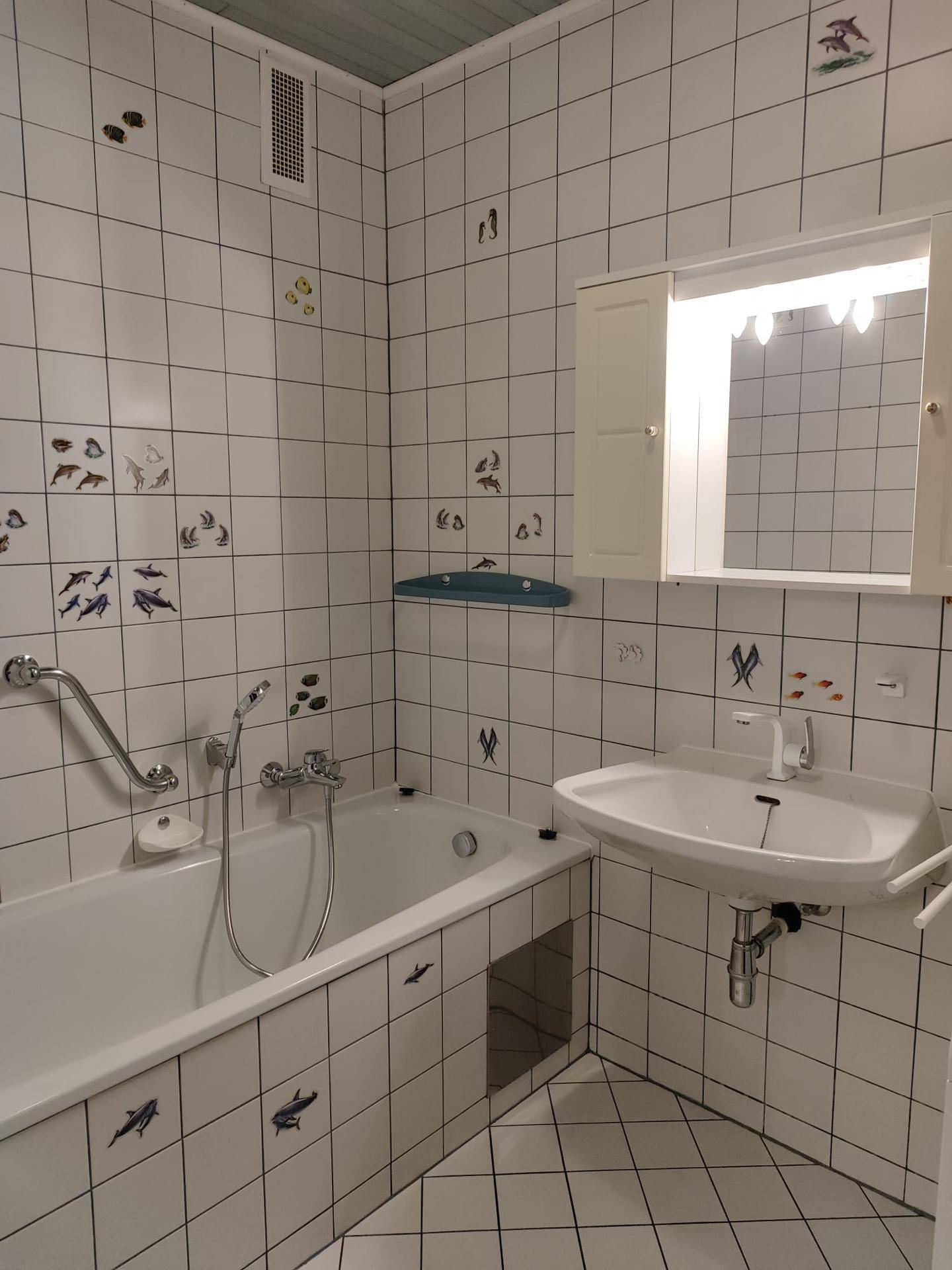 Badezimmer mit Badewanne, Waschbecken, Spiegel und weiß gefliesten Wänden.
