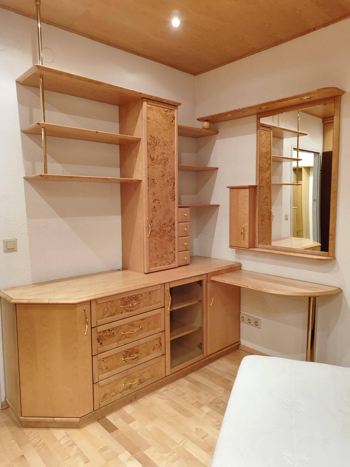 Schlafzimmer mit hellem Holzmobiliar, Regalen, Spiegel und integriertem Schreibtisch.