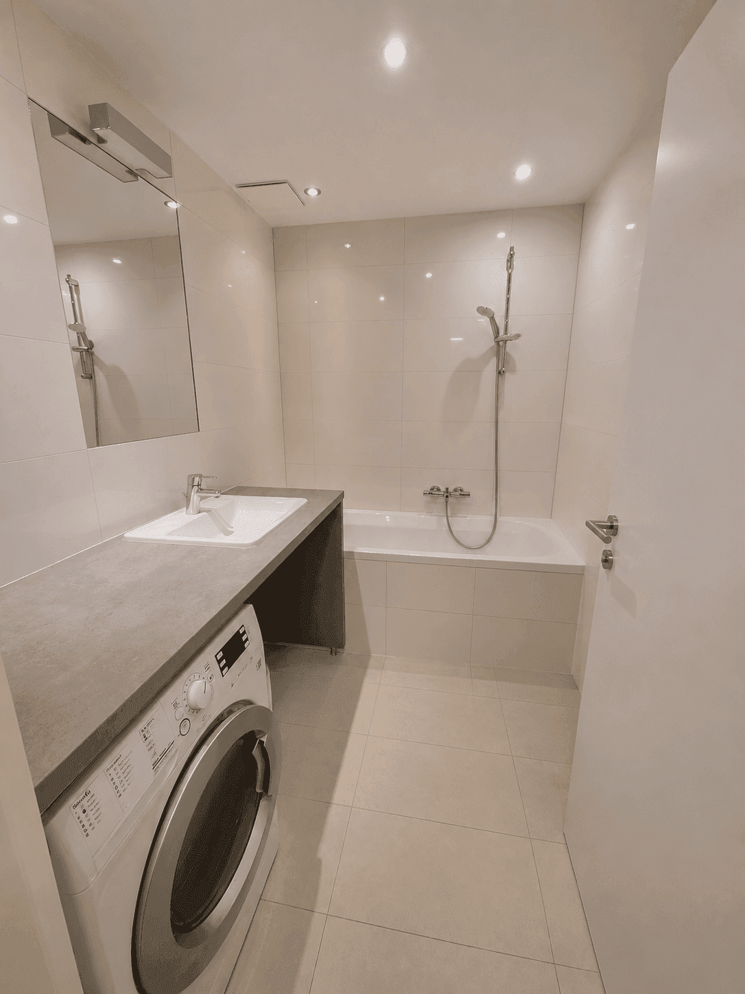 Helles Badezimmer mit Badewanne, Waschbecken, Spiegel und integrierter Waschmaschine.