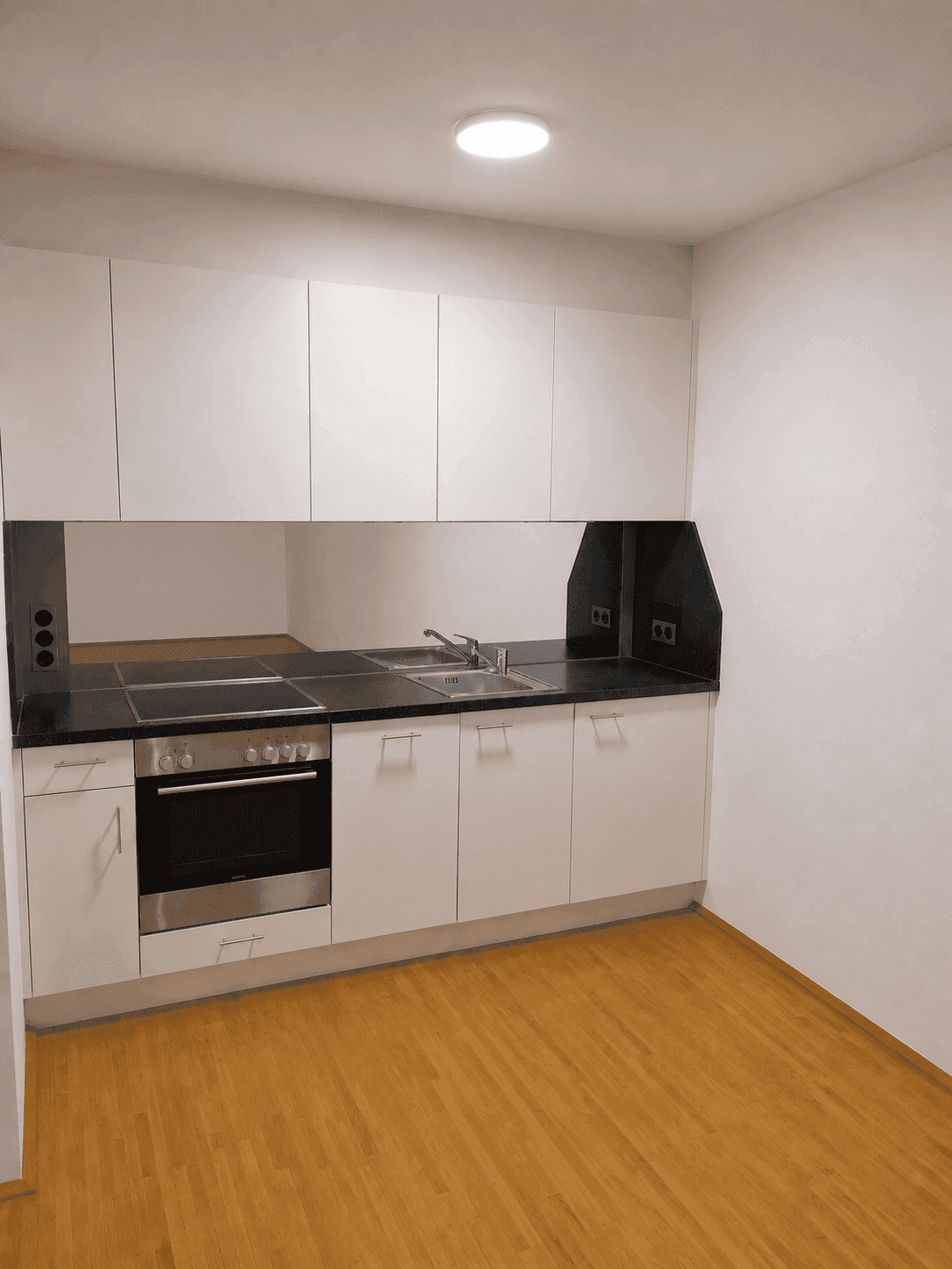Moderne Einbauküche mit weißen Schränken, schwarzer Arbeitsplatte und integrierten Geräten.