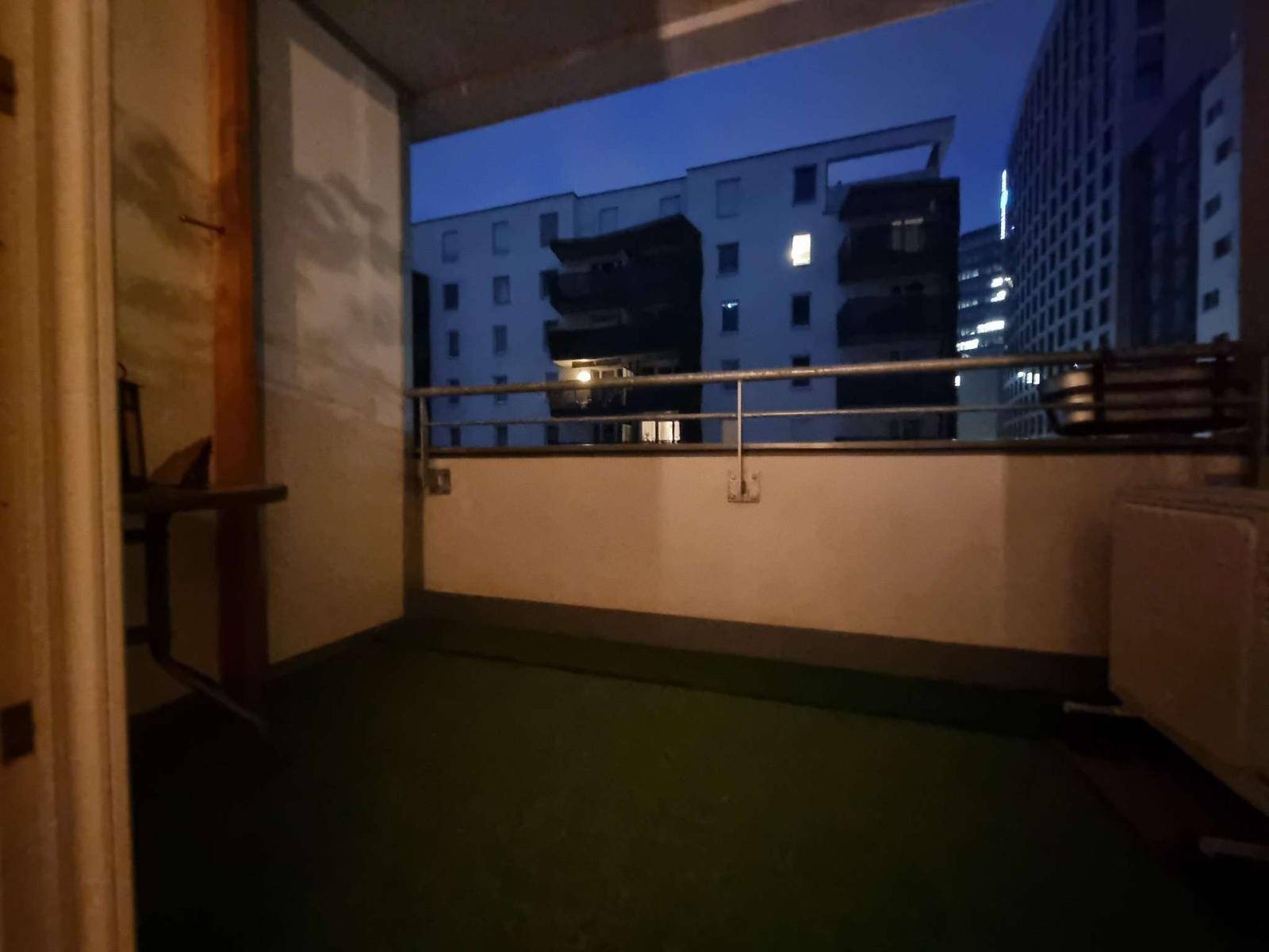 Balkon mit Kunstrasen und Blick auf umliegende Wohngebäude in der Nacht.