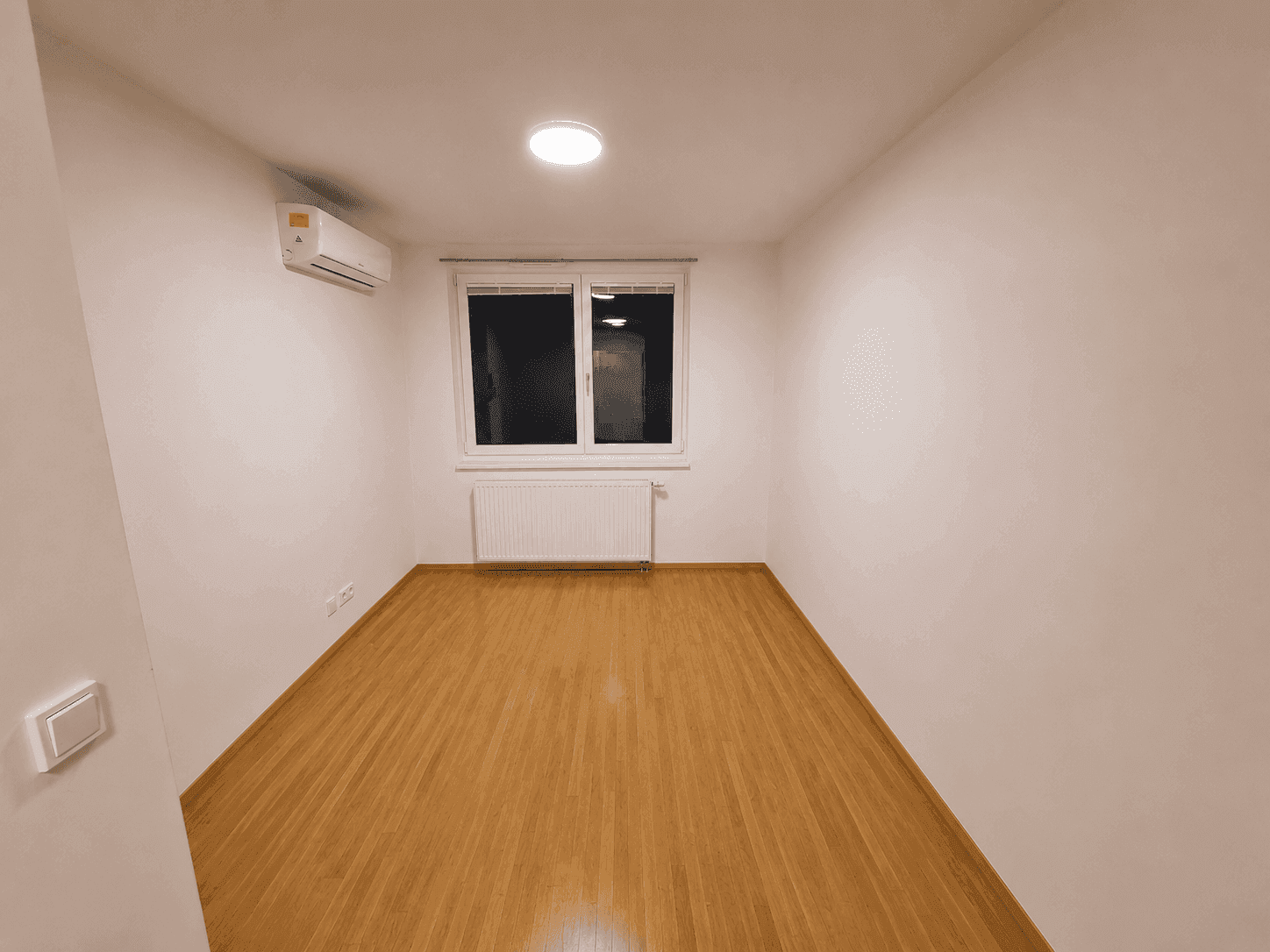 Helles Zimmer mit Parkettboden, Klimaanlage und Fenster, ideal als Schlafzimmer.