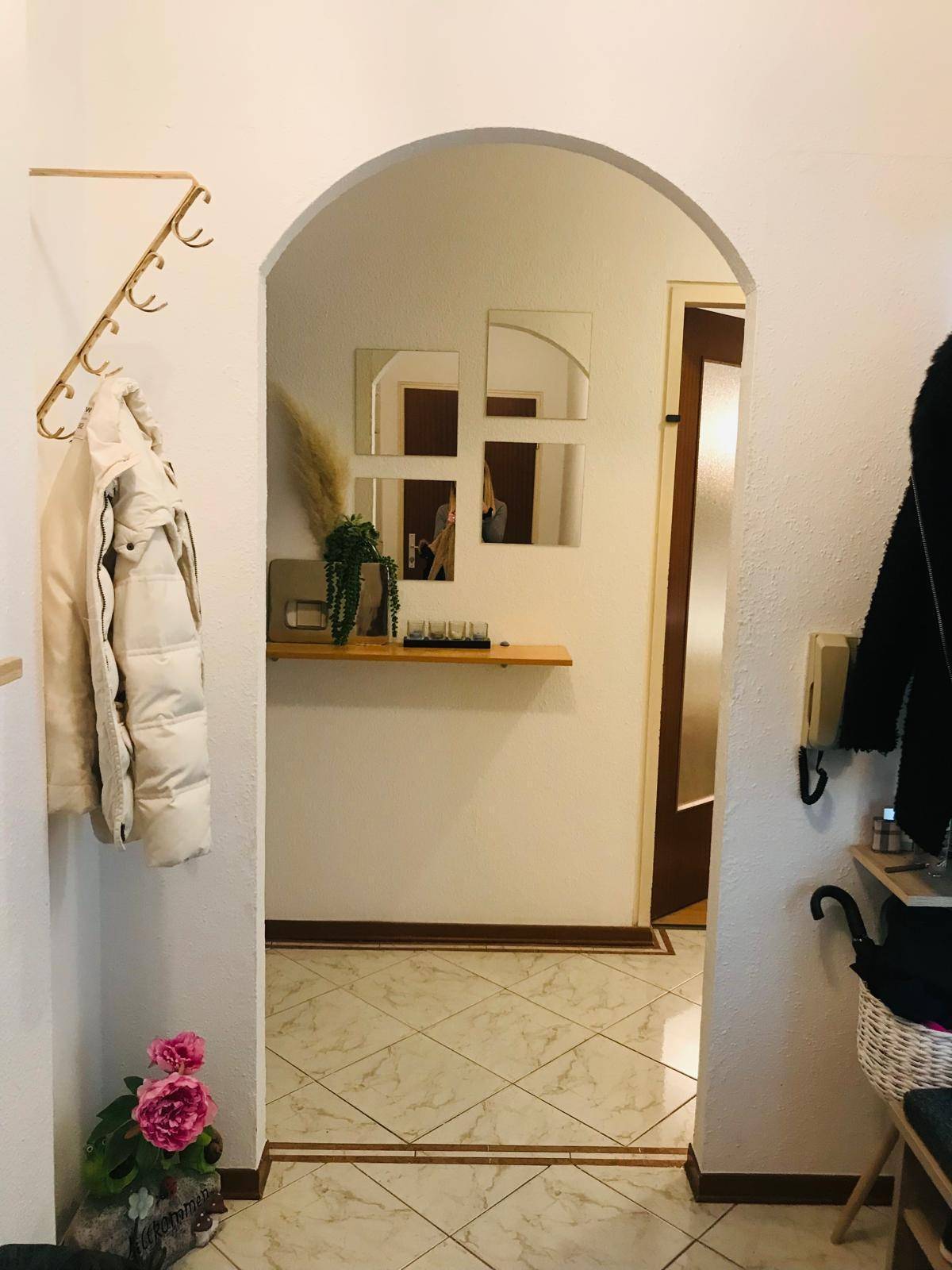 Eingangsbereich mit Fliesenboden, Garderobe und dekorativem Spiegel über einem Regal.