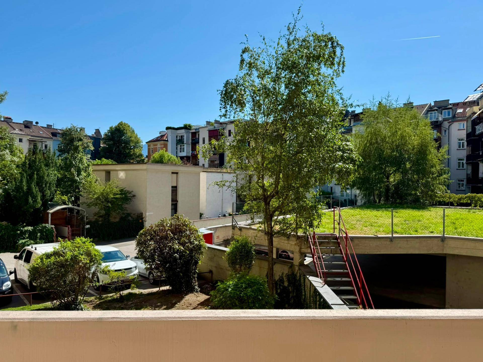 Weitläufiger Blick vom Balkon auf die grüne Umgebung und die angrenzenden Wohngebäude.