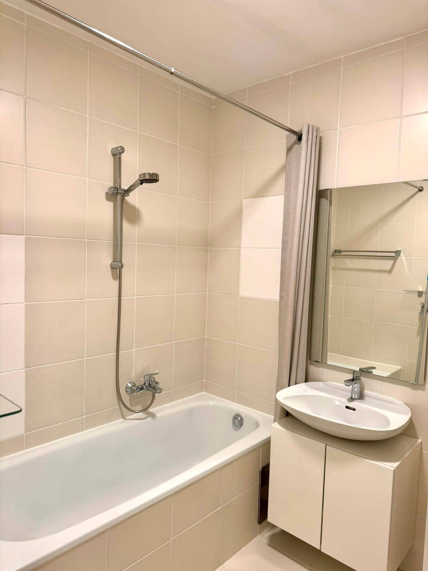 Helles Badezimmer mit Badewanne, Duschvorrichtung und modernem Waschbecken.