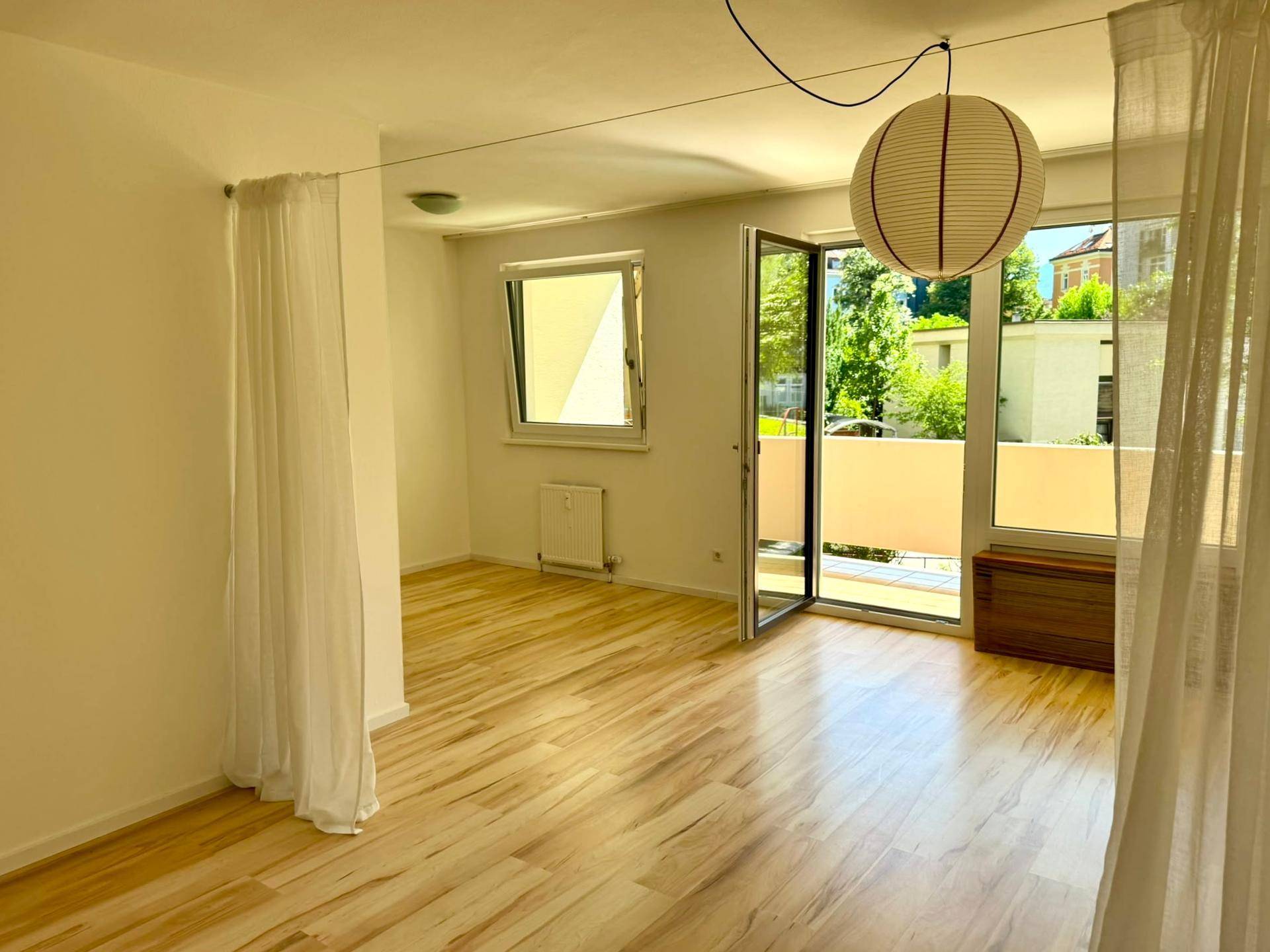 Geräumiges, leeres Zimmer mit hellem Holzboden und direktem Zugang zum Balkon.
