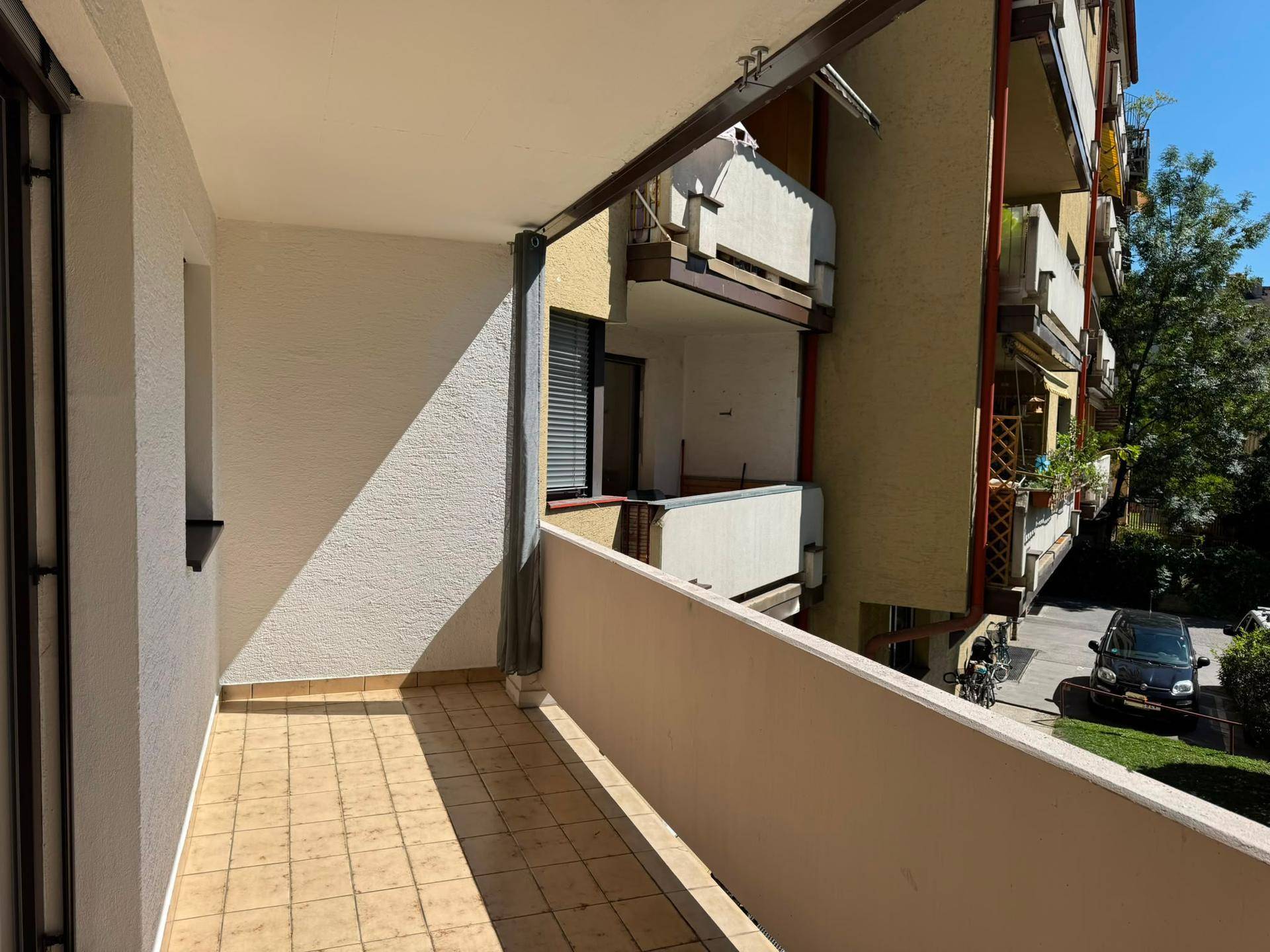 Geräumiger Balkon mit Fliesenboden und Blick auf die Straße und Nachbargebäude.